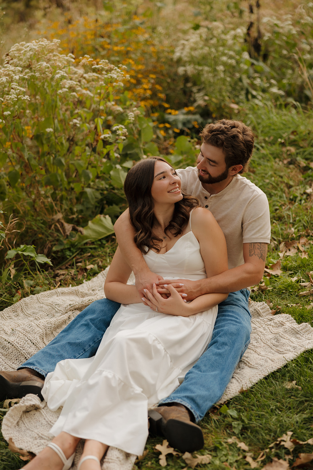 Couple sitting on a blanket in a wildflower-filled meadow near Madison WI, gazing at each other with soft smiles.