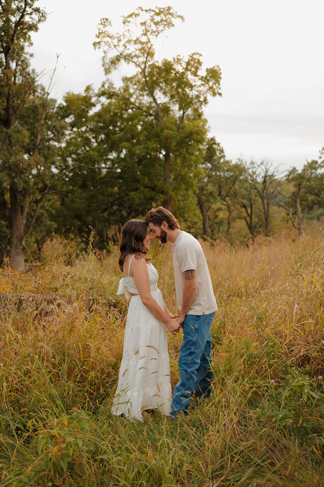 Couple holding hands and touching foreheads in a peaceful field near Madison WI, surrounded by tall autumn grass.