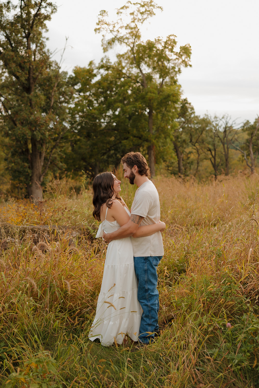 Engagement photo of a couple wrapped in an embrace, standing in a dreamy Madison WI field with soft fall colors.