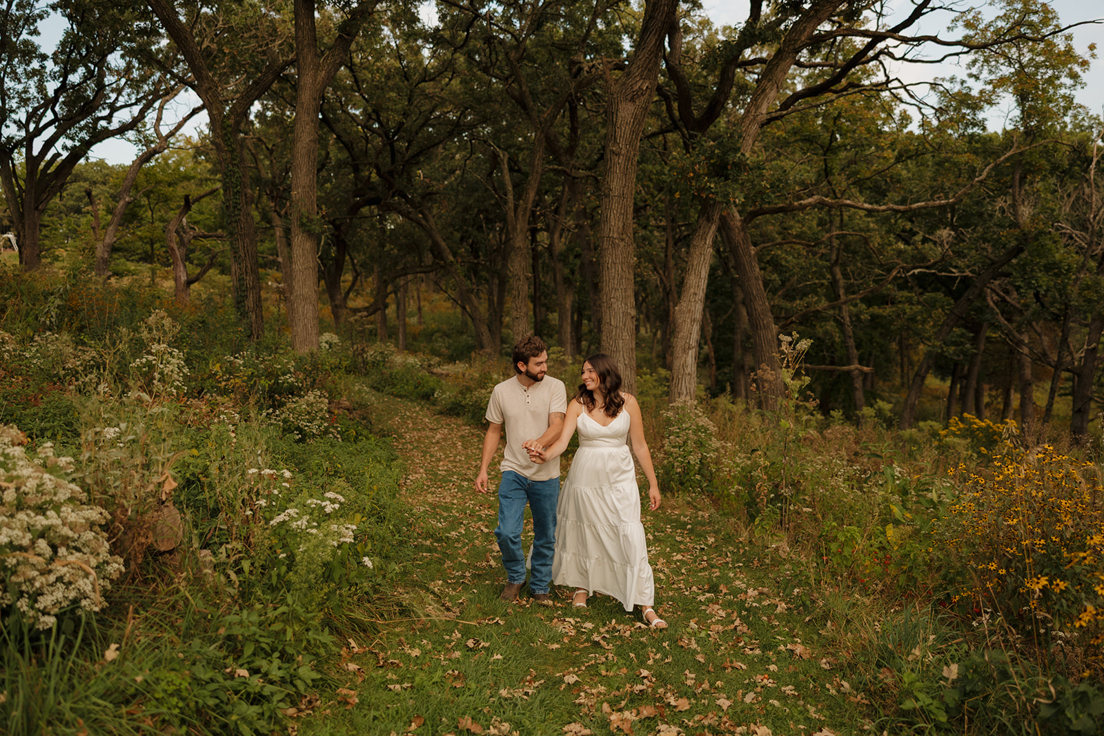 Engagement photo of a couple walking hand-in-hand through a forest trail near Madison WI, glowing with connection.