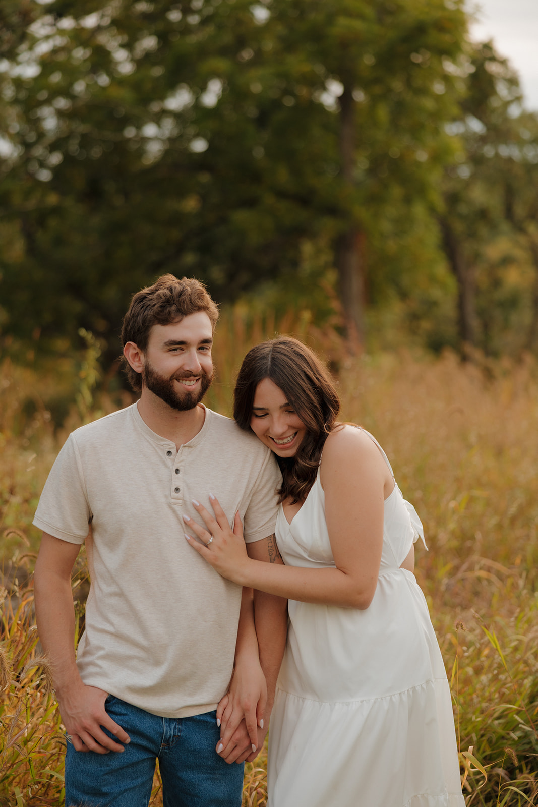 Bride-to-be resting her head on her fiancé’s shoulder in a Madison WI prairie, both glowing with joy.