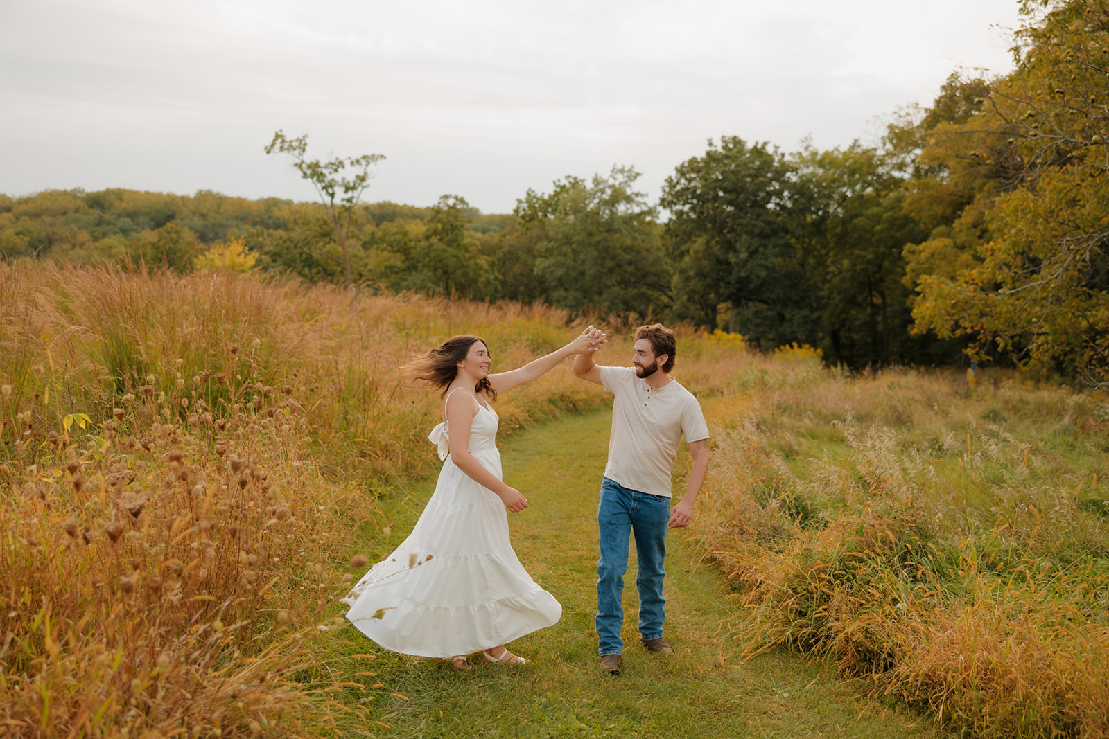 Couple dancing along a grassy trail near Madison WI, surrounded by golden prairie grass and soft evening light.
