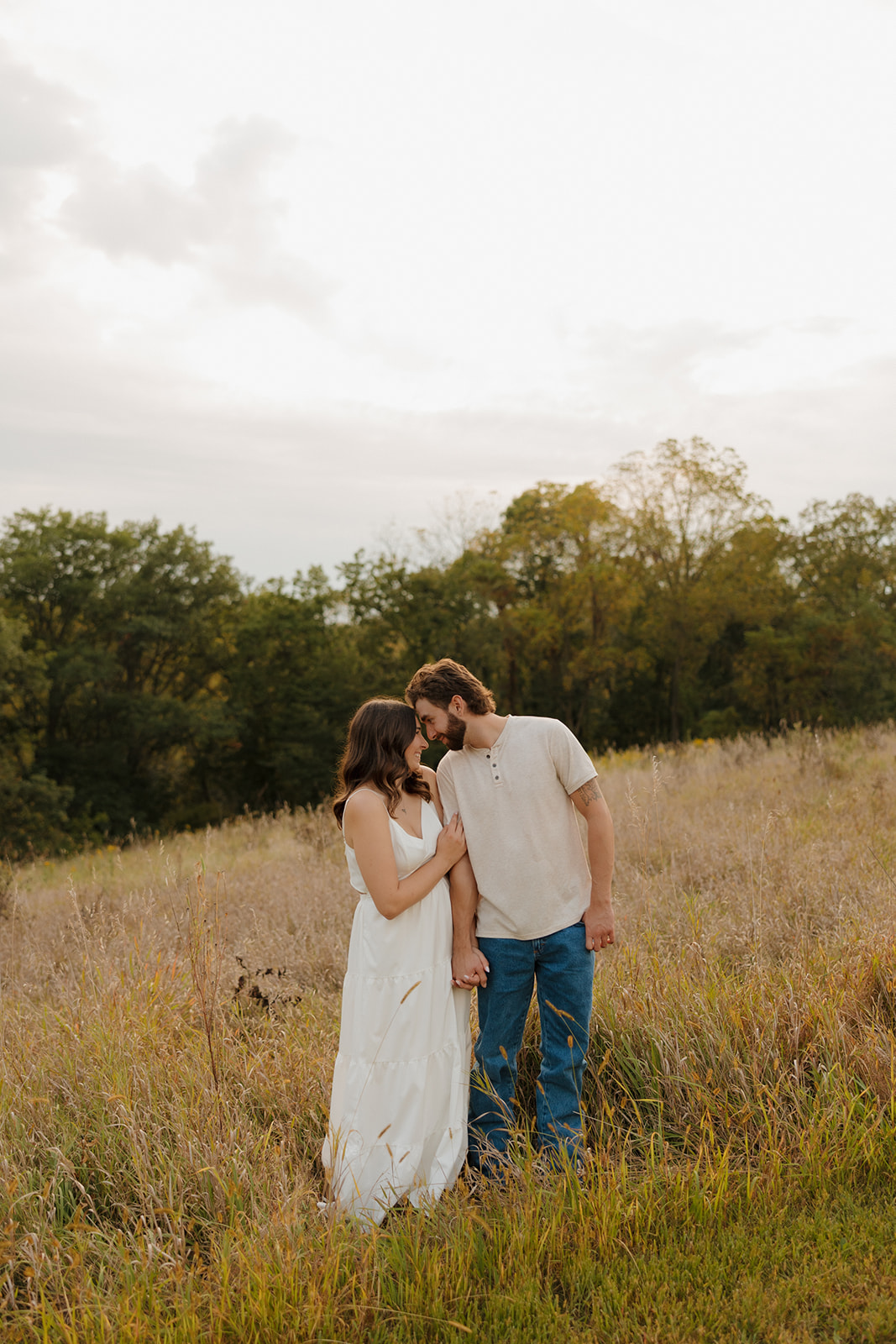 Romantic moment of a couple kissing in the middle of a windswept Madison WI meadow, just before sunset.