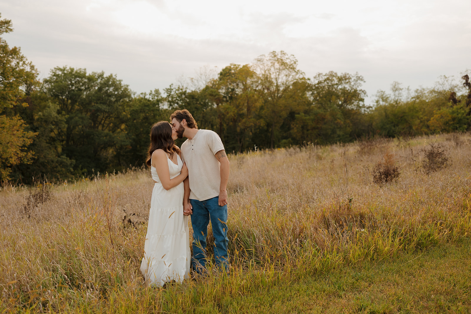 Engaged couple sharing a kiss in a golden meadow just outside Madison WI, holding hands as the sun sets.
