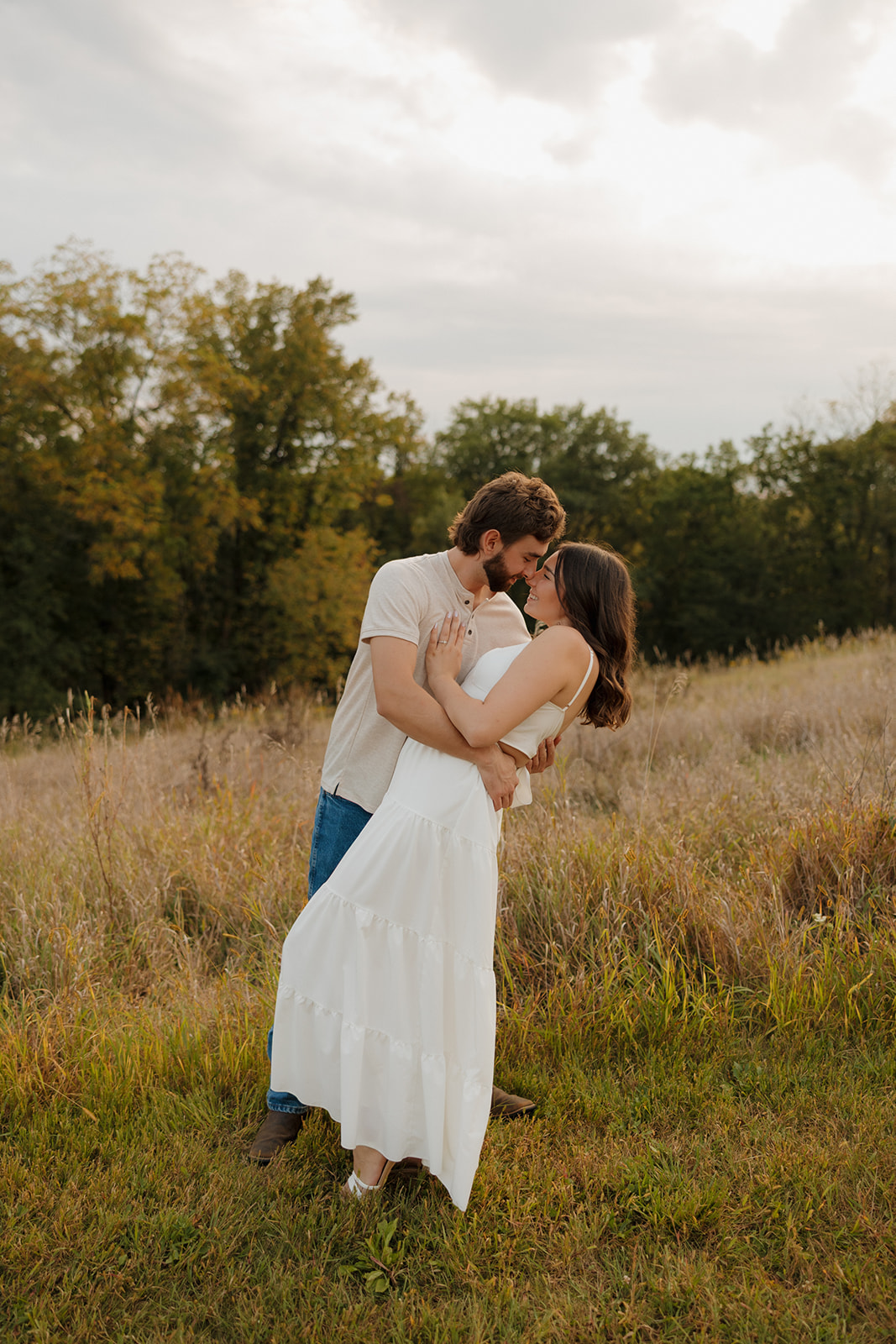 Playful couple sharing a kiss in a sunlit meadow near Madison WI during golden hour.