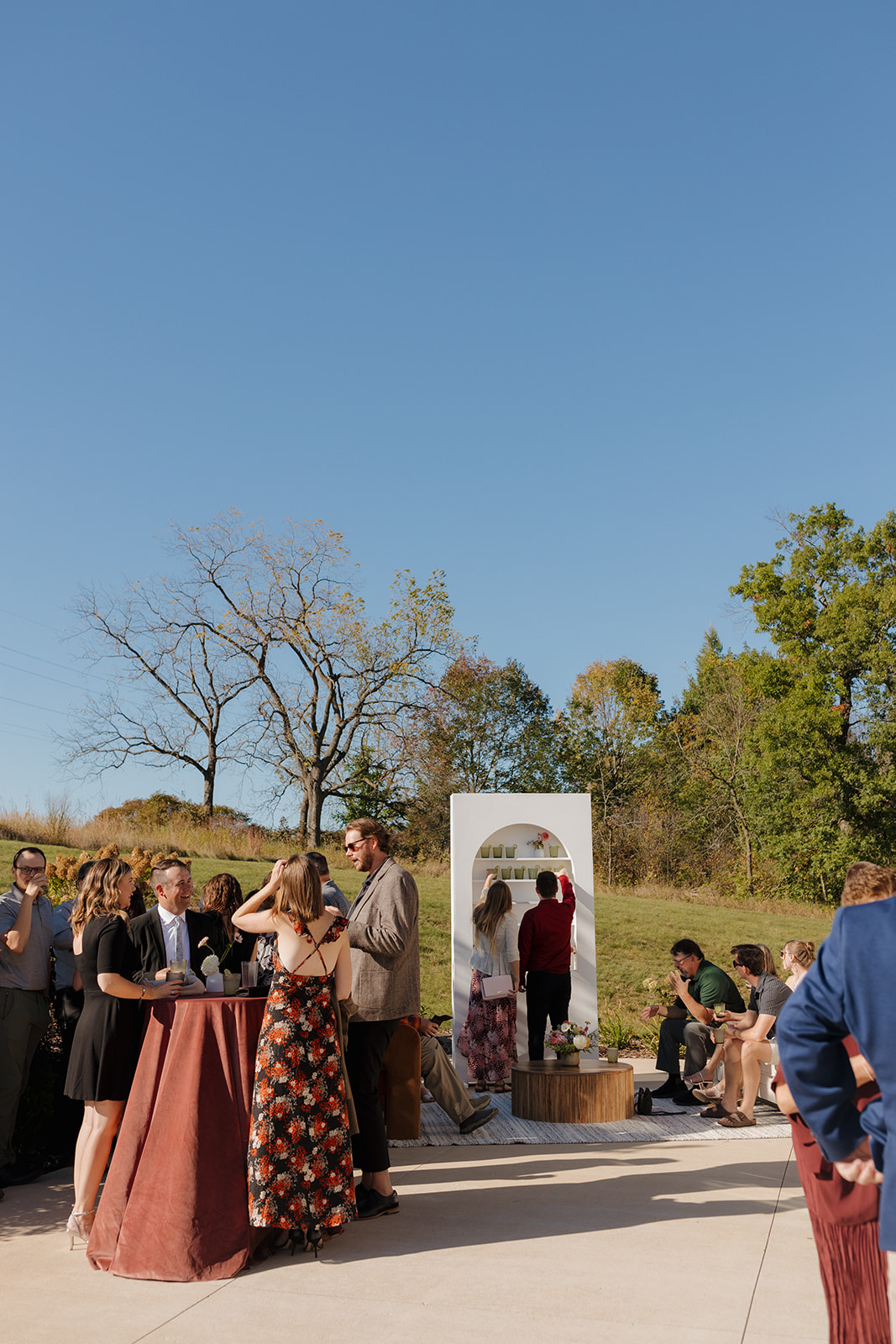 Guests chatting and sipping drinks during outdoor cocktail hour under a clear blue sky at a wedding venue in Wisconsin.