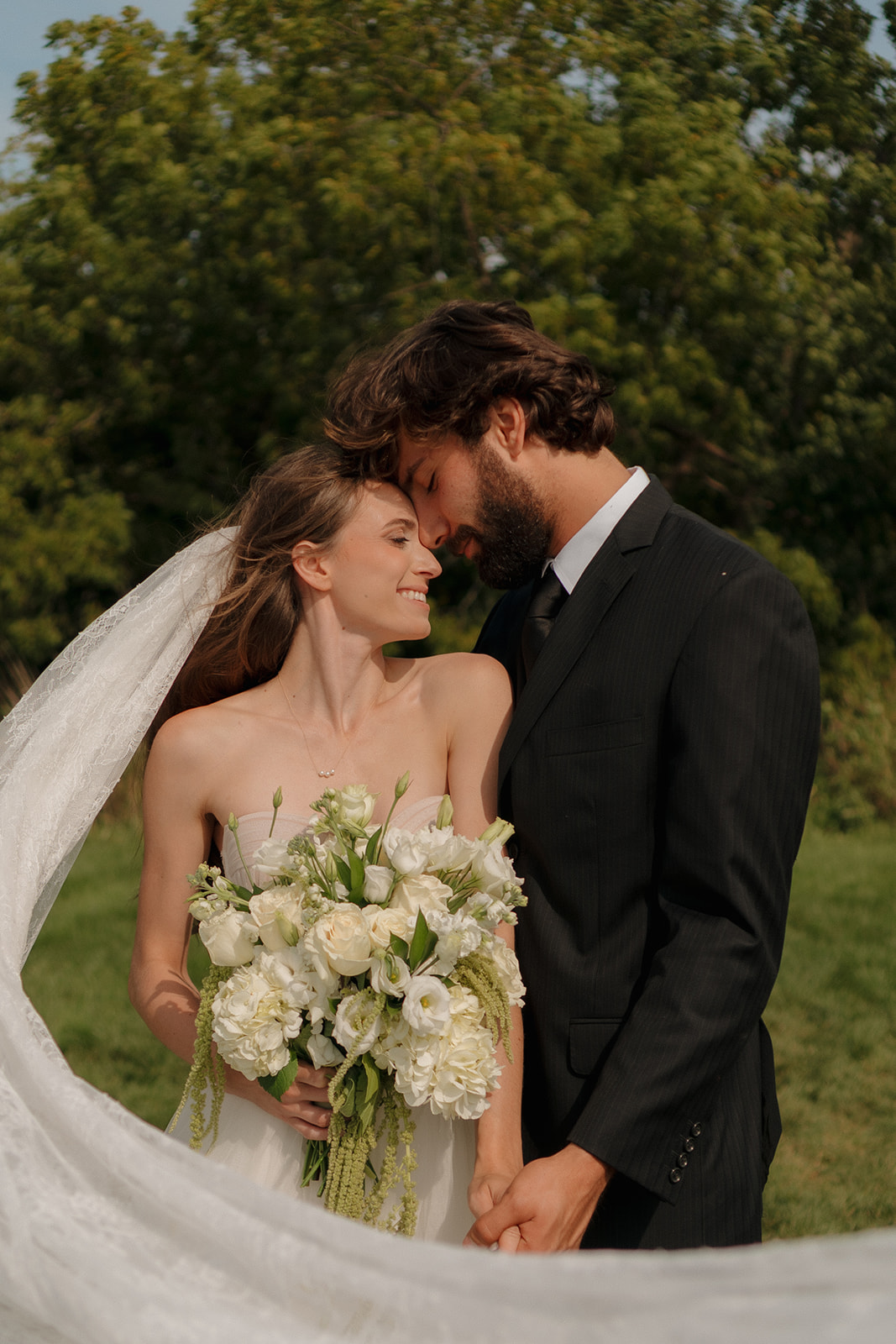 Romantic close-up of the couple wrapped in each other’s arms outside their venue, veil flowing behind and smiles all around.