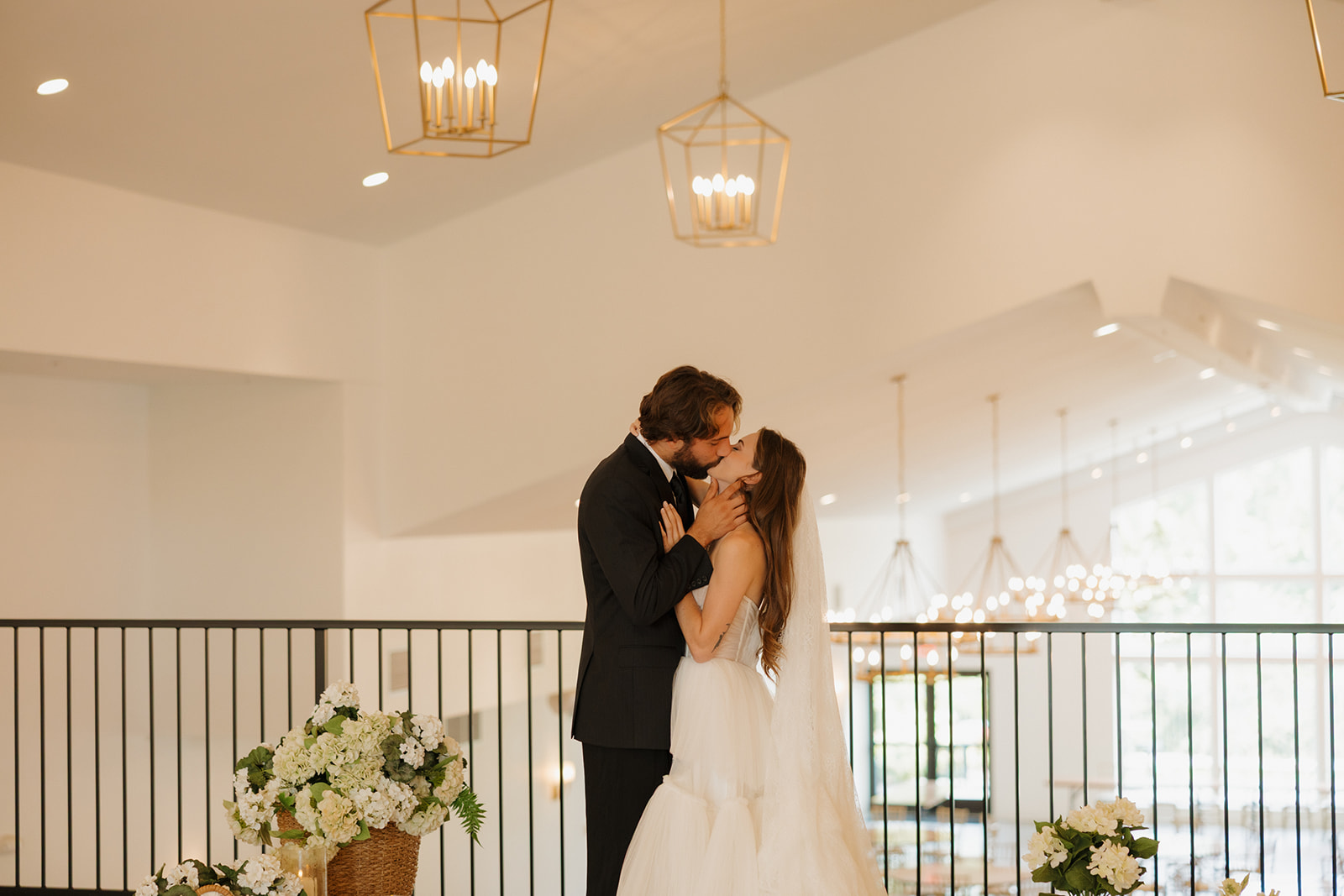 Indoor kiss with florals flanking the couple and golden light overhead, captured with elegance and intimacy.