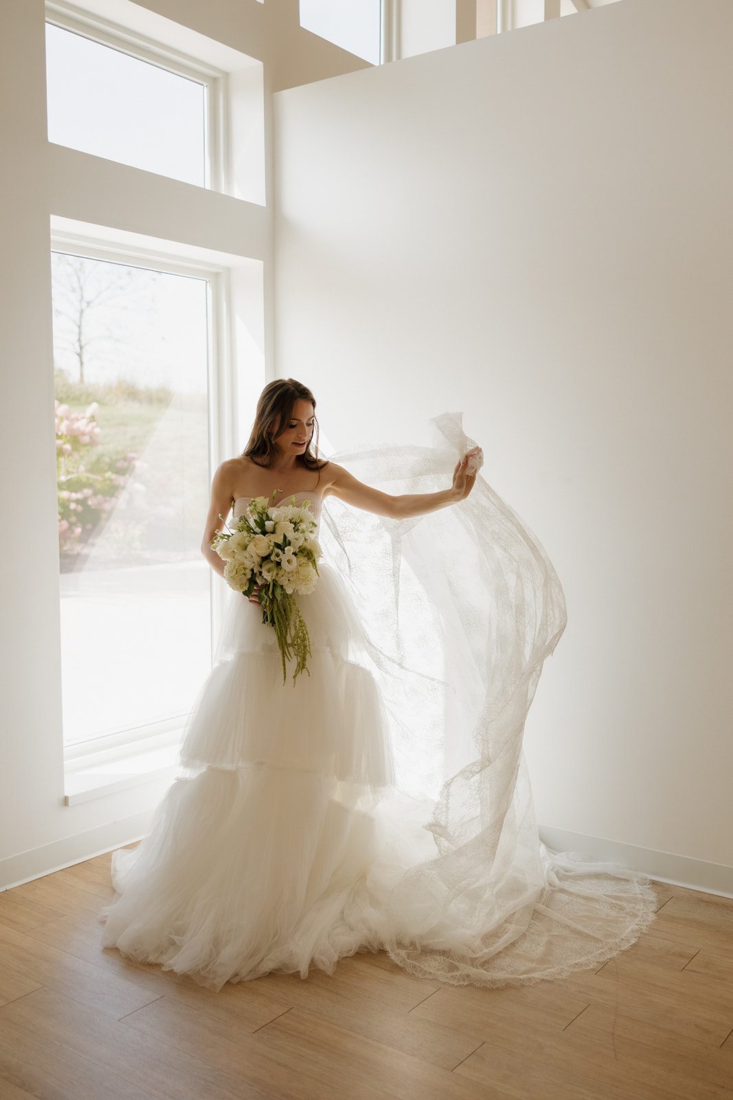 Bride twirling her lace veil in sun-drenched window light, holding a classic bouquet—an effortlessly graceful moment from weddings in Wisconsin.