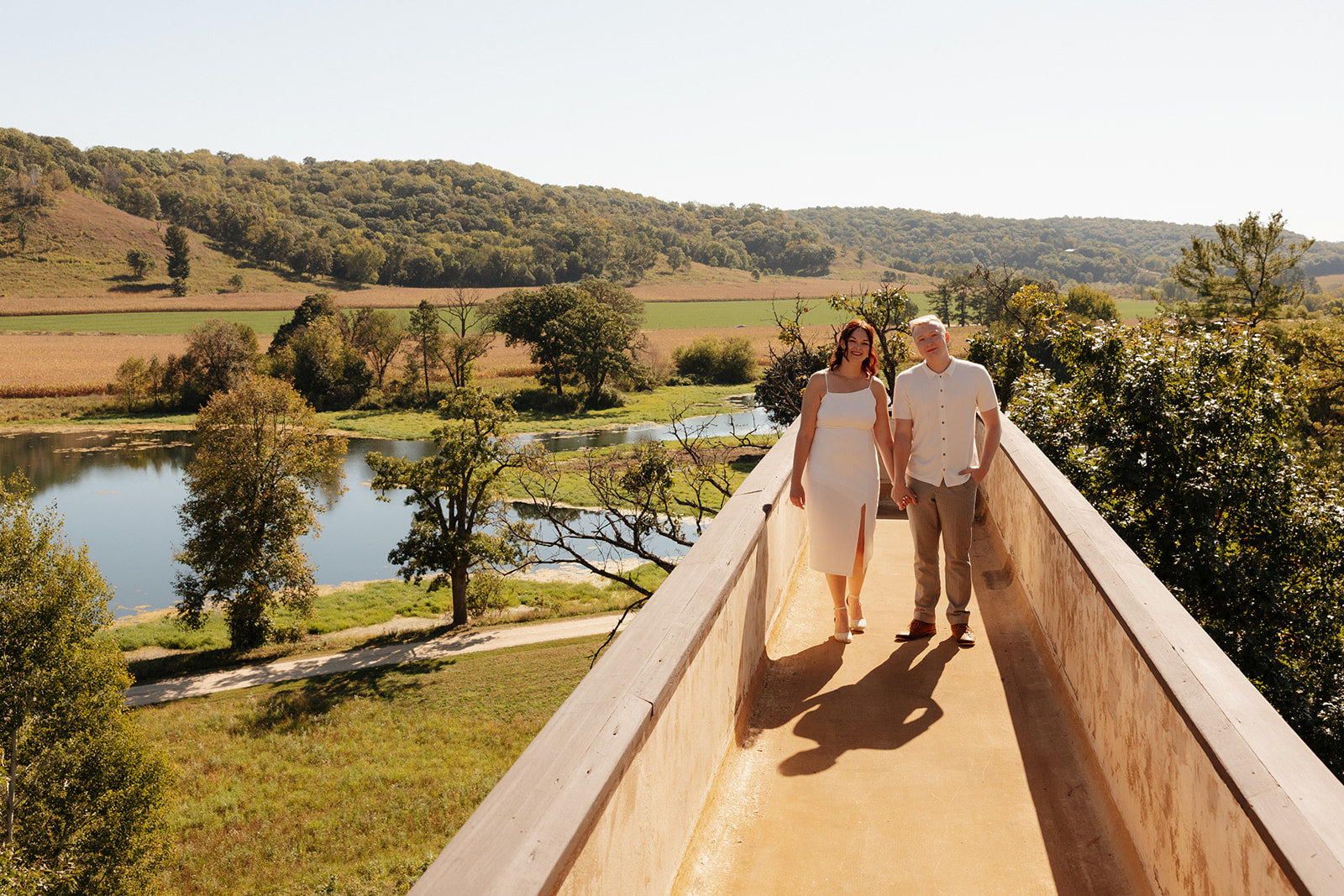 Couple walking hand in hand on a scenic overlook path with panoramic river valley views—an elevated and intentional idea for engagement photos.