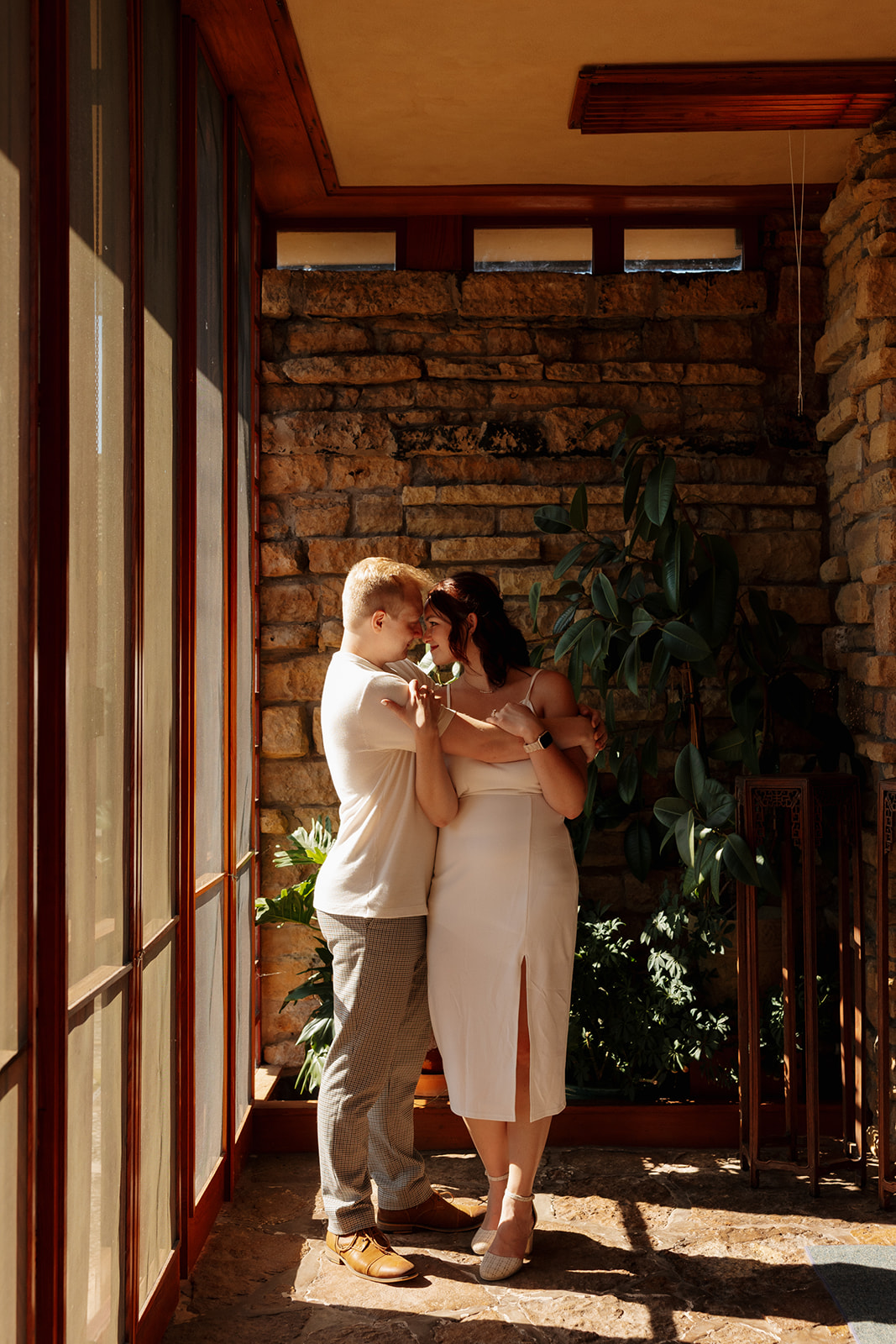 A quiet, romantic moment as the couple shares a forehead touch in a corner filled with natural light, stone textures, and greenery.