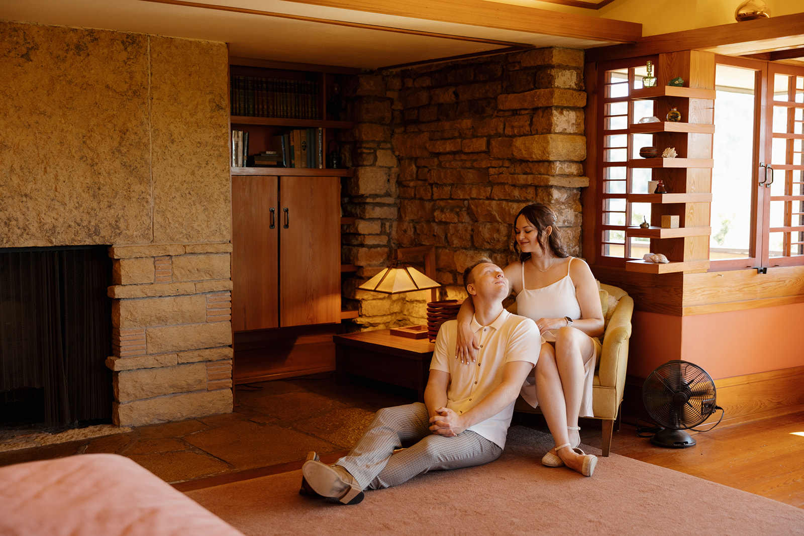 Couple cozying up in a reading nook, with warm lighting, vintage charm, and earthy textures—an at-home vibe that makes a sweet and relaxed idea for engagement photos.