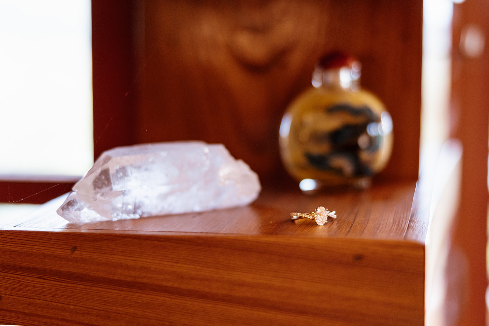 A close-up of an engagement ring placed on a wooden shelf next to a crystal and antique bottle, perfectly styled for detail shots with personality.
