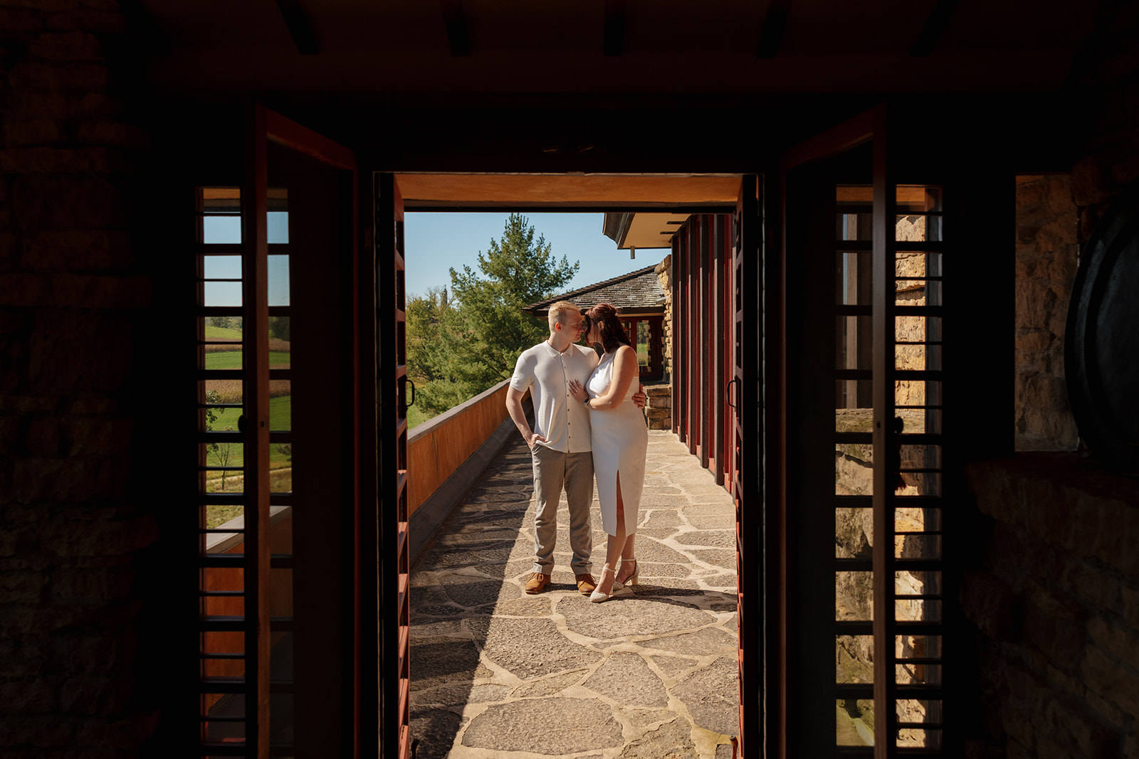 Framed in a shadowed stone doorway, the couple shares a soft gaze under golden light—an architectural idea for engagement photos full of texture and contrast.