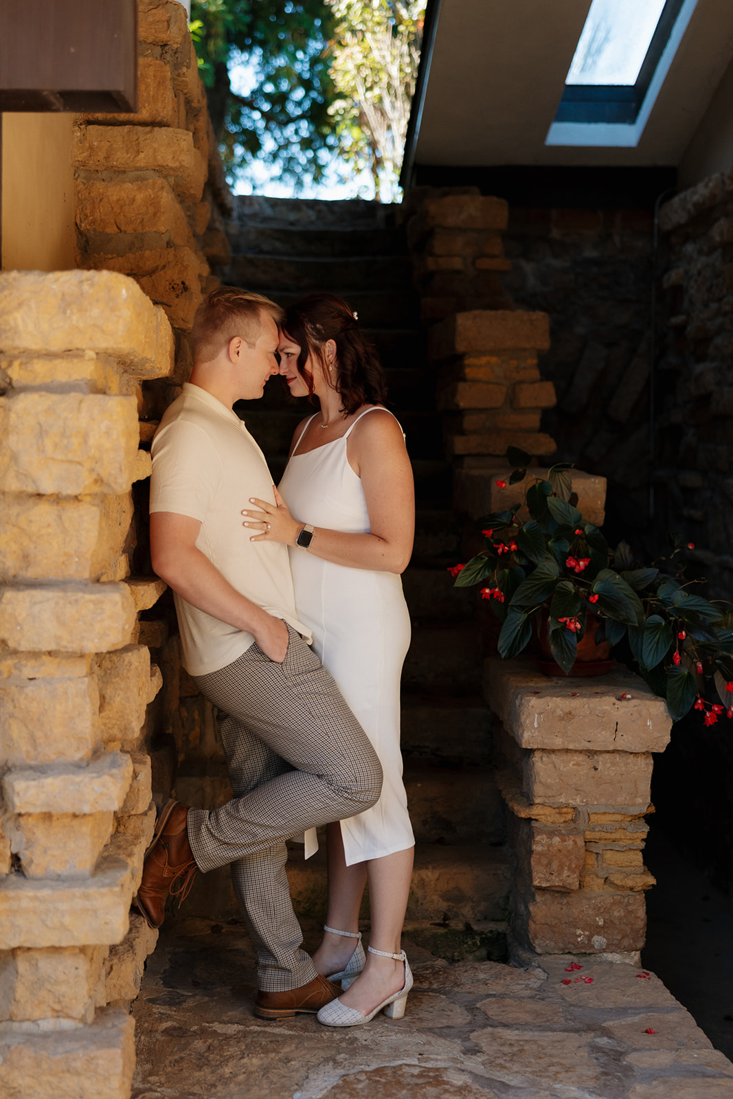 Couple nestled together between stone walls, sharing an intimate moment in a rustic-modern architectural space.