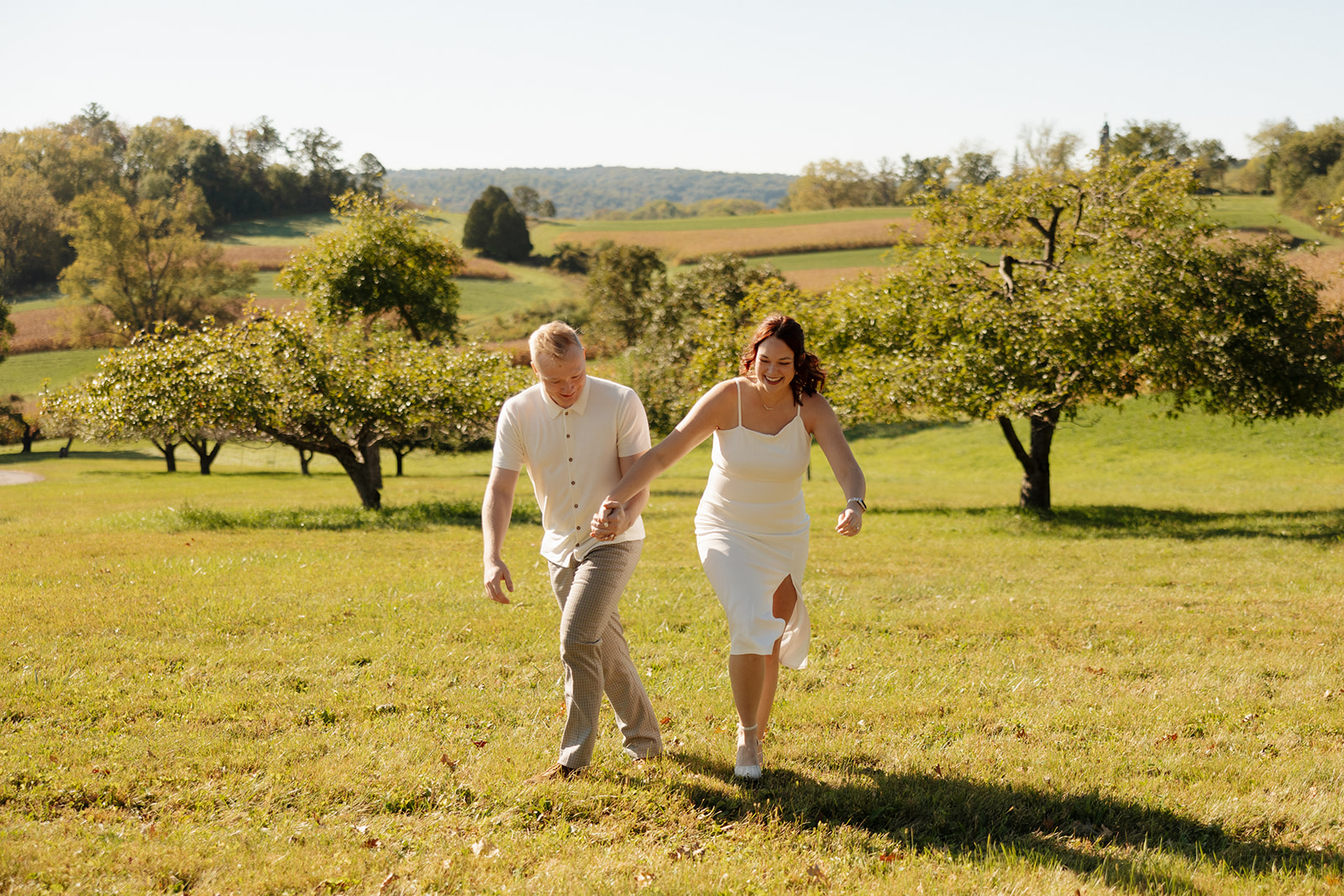 Laughing and running uphill through a wide-open field, the couple radiates joy and movement—one of the most playful ideas for engagement photos.