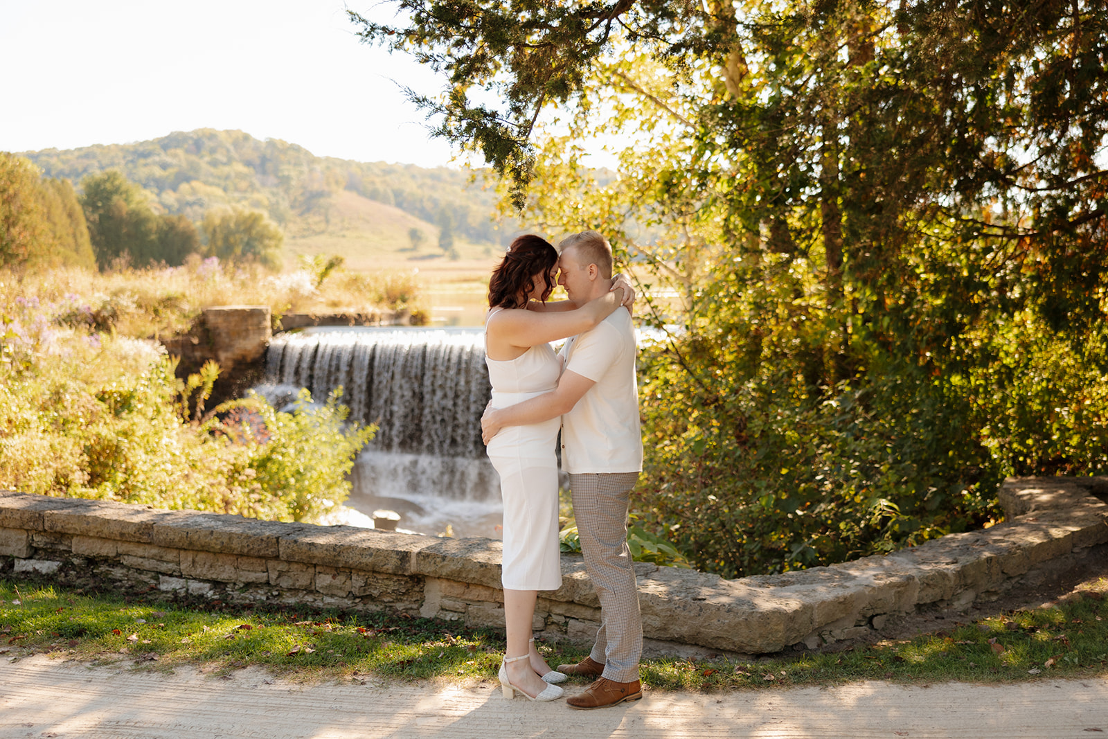 Couple embracing in front of a waterfall, surrounded by wild greenery and golden afternoon light—a romantic, outdoorsy idea for engagement photos.