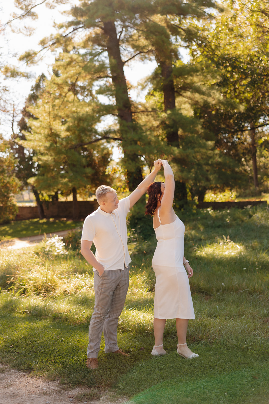 Dancing in the dappled light—he twirls her under towering trees, making for a playful and natural idea for engagement photos in a wooded setting.