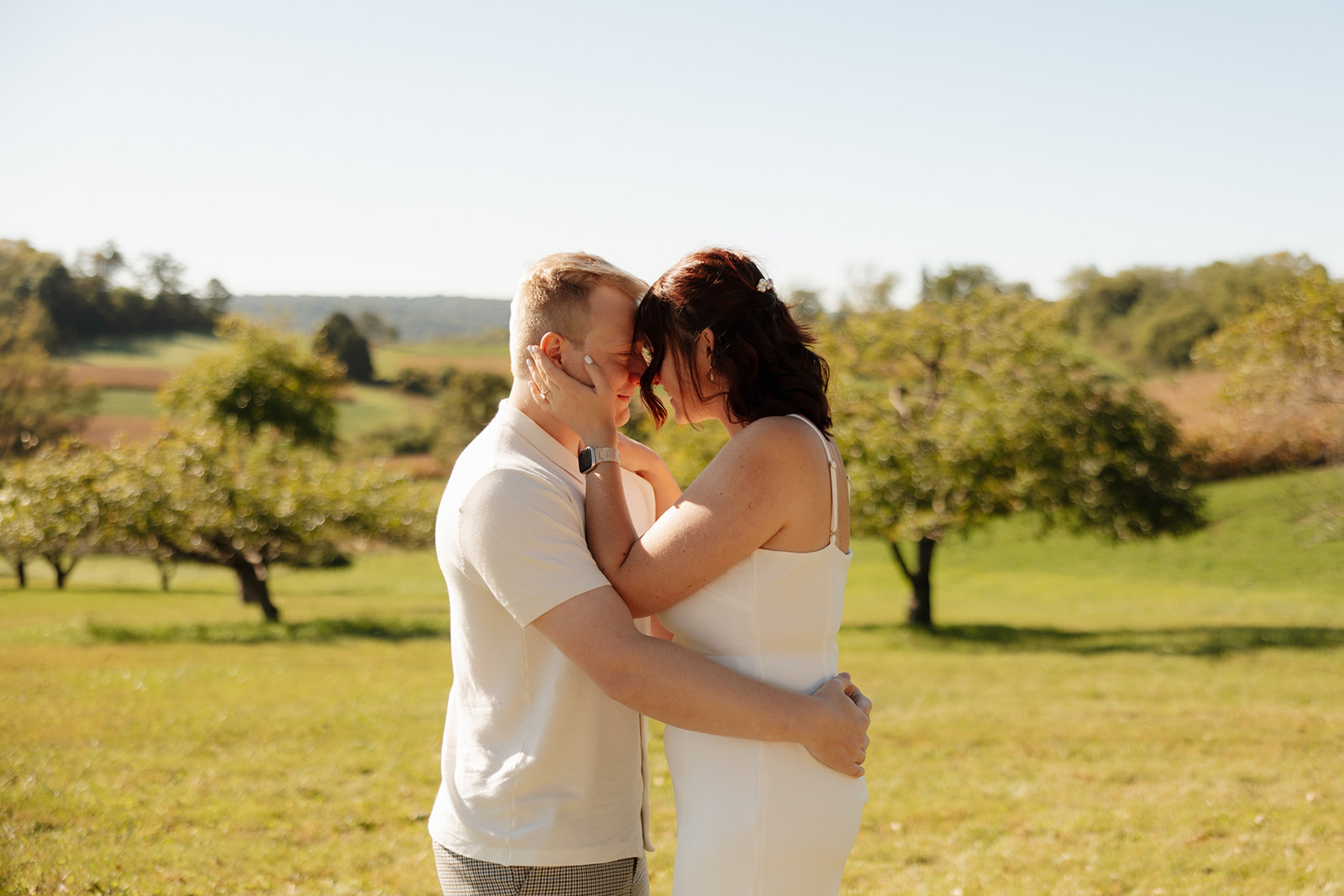 Foreheads touching and hands cupping each other’s faces, this couple shares an intimate moment in a sunlit field—an effortlessly romantic idea for engagement photos.