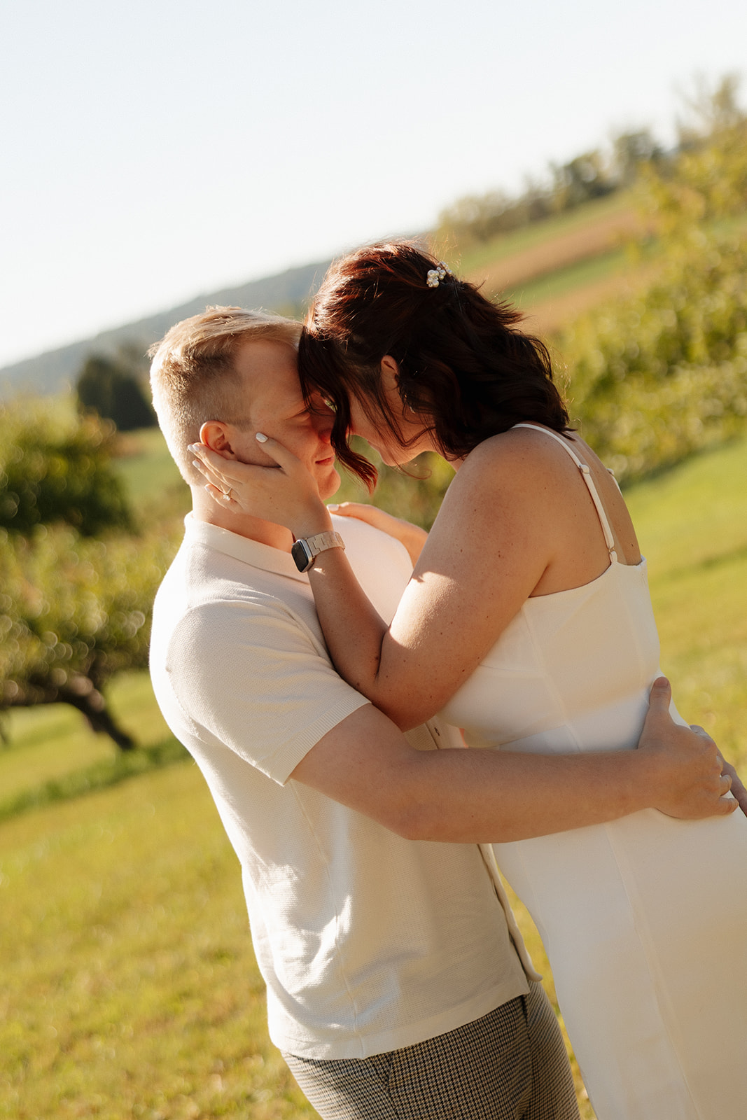 Romantic moment in a sun-drenched field, with the couple wrapped in a gentle forehead-to-forehead embrace. A dreamy idea for engagement photos with warm light and golden hour magic.