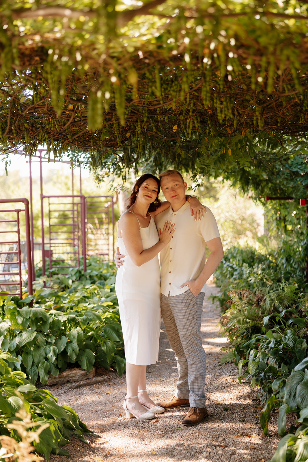 Nestled beneath a leafy canopy, the couple poses together with relaxed smiles—an enchanting idea for engagement photos in a garden-like hideaway.
