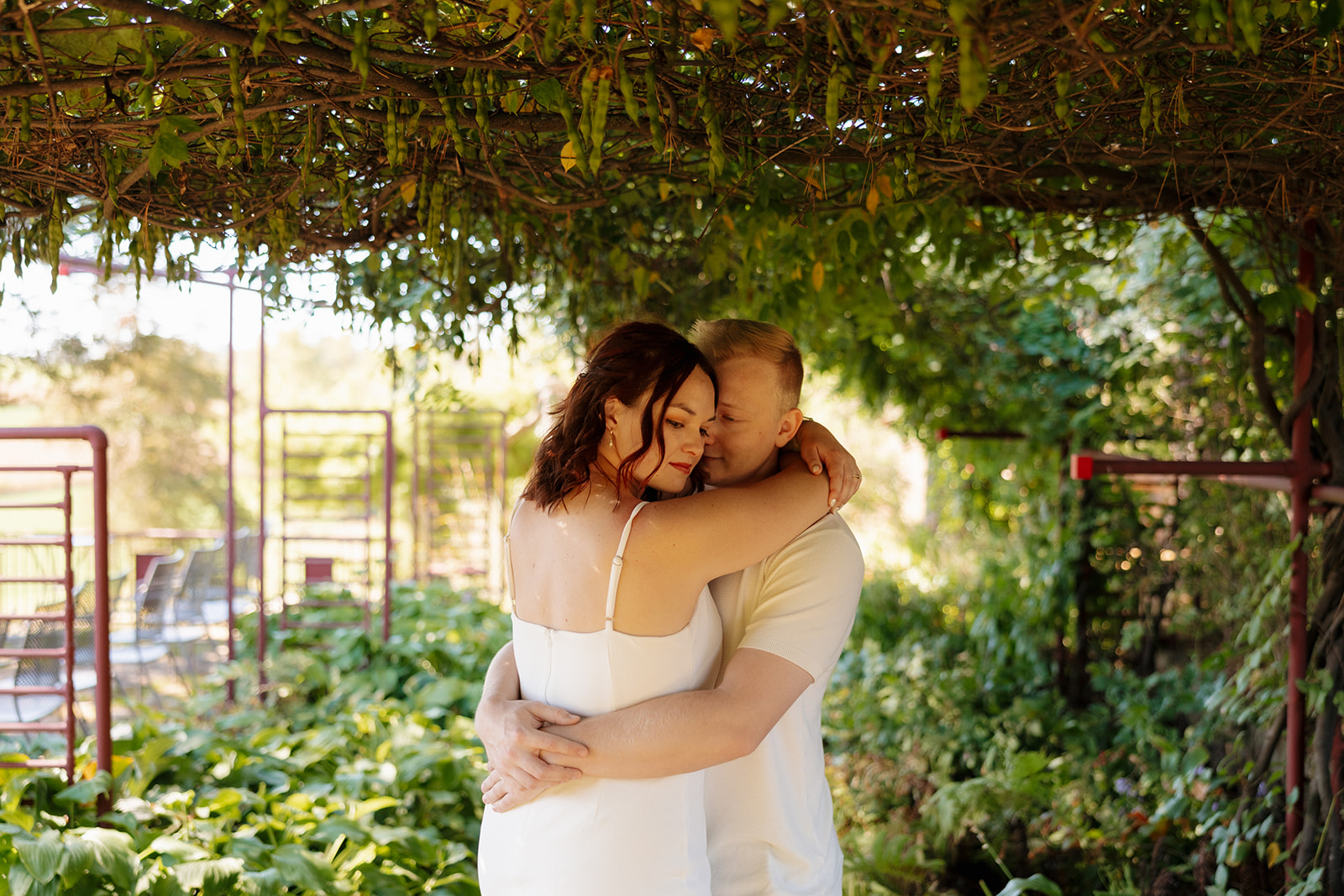 Under a lush green arbor, the couple shares a tender hug surrounded by greenery—an earthy, emotionally rich idea for engagement photos with cozy vibes.