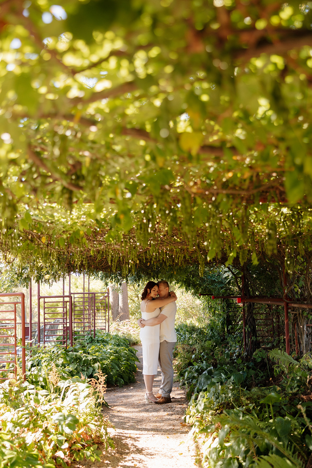 Under a lush green canopy, the couple hugs on a winding garden path—an enchanting and whimsical idea for engagement photos.