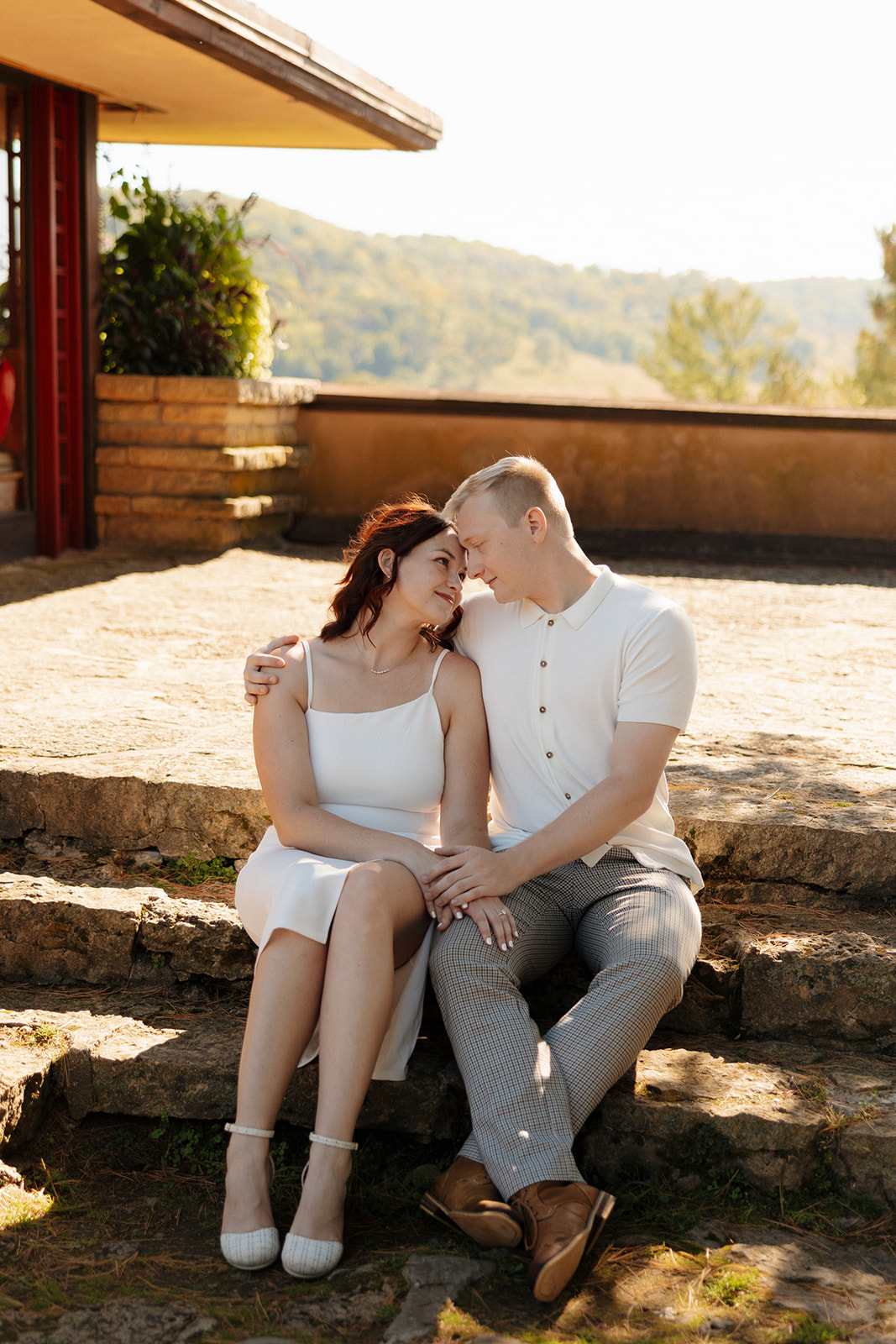 Couple sitting forehead-to-forehead on stone steps with warm, golden light around them, creating a relaxed and romantic feel.