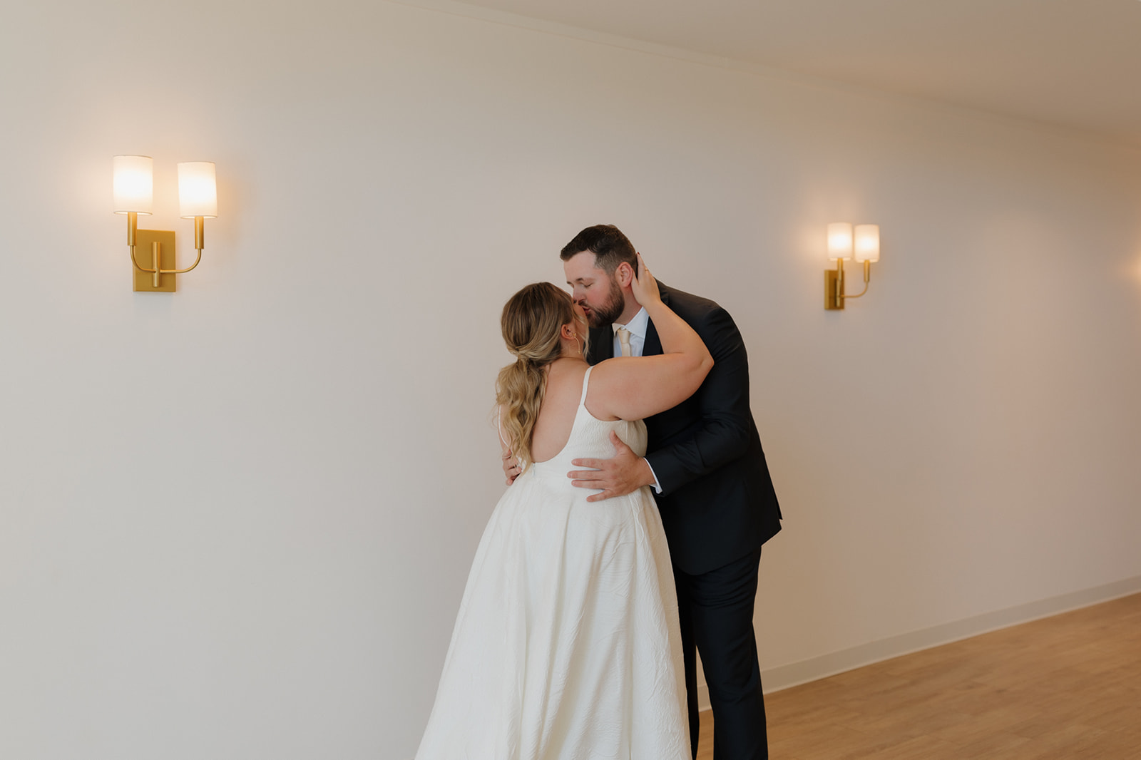 A first kiss shared against a white wall with golden sconces, full of tenderness and anticipation.