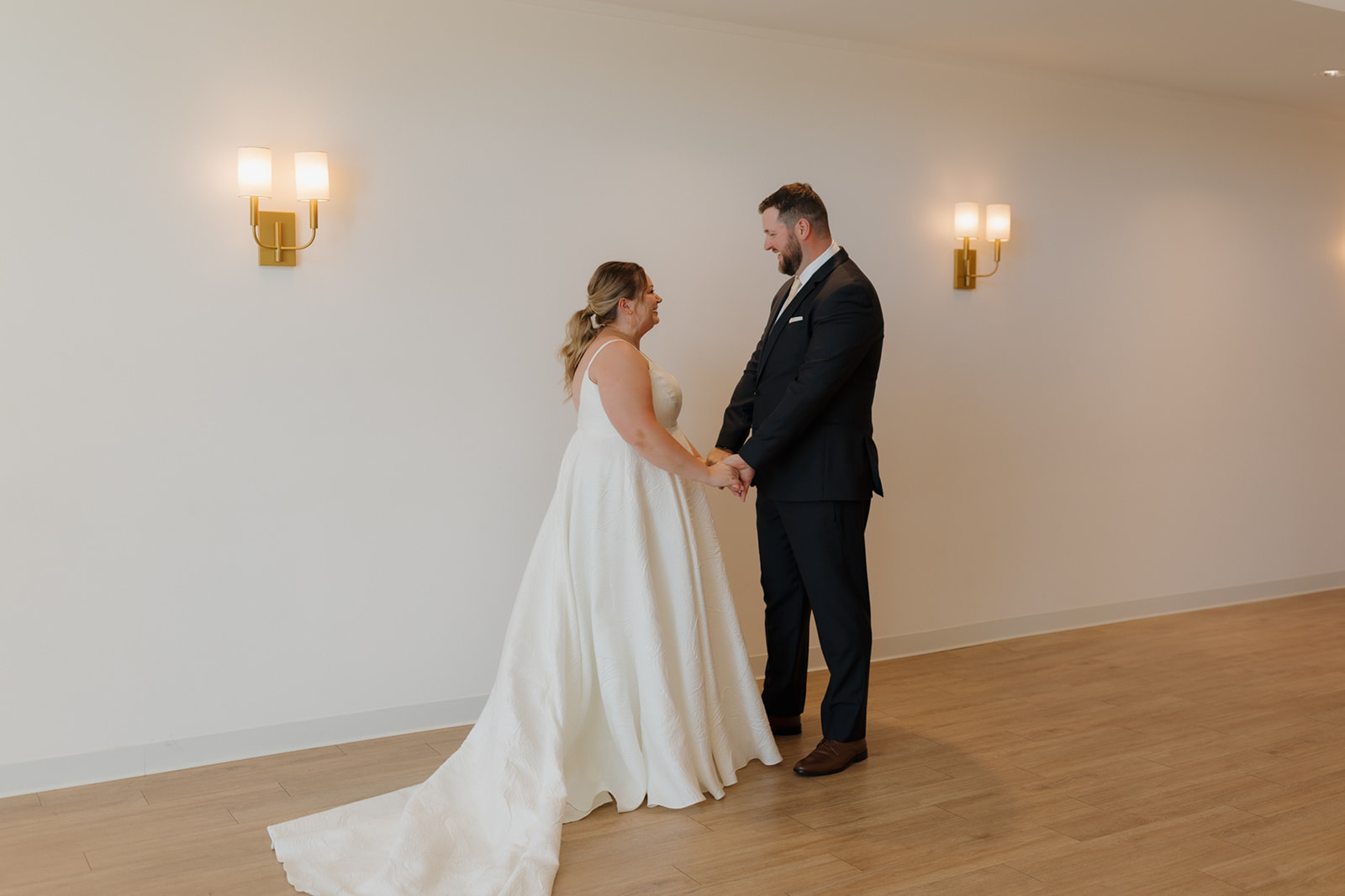 Bride and groom holding hands and smiling during their private first look at a bright wedding venue in Wisconsin.