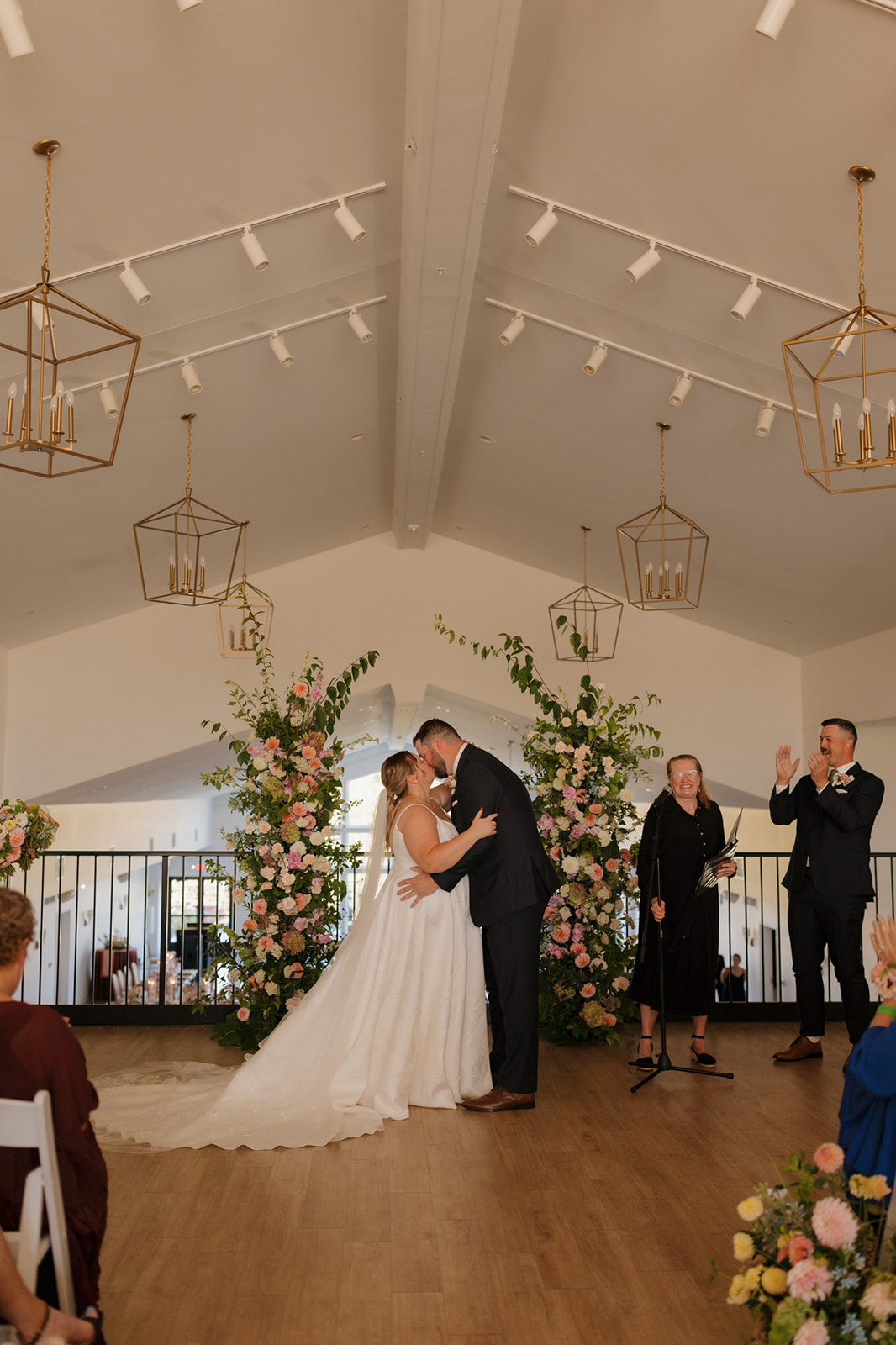 Indoor ceremony kiss under modern gold chandeliers and lush floral installations at a wedding venue in Wisconsin.