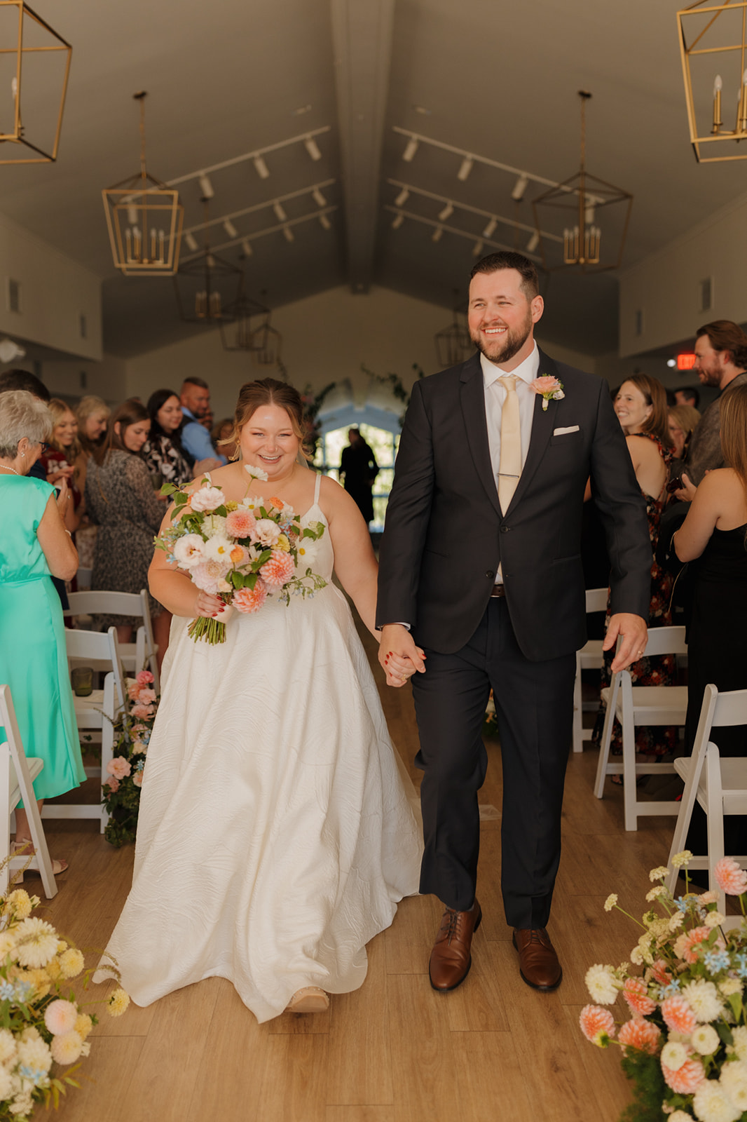 Bride and groom beaming as they walk back up the aisle hand in hand, just married at a wedding venue in Wisconsin.
