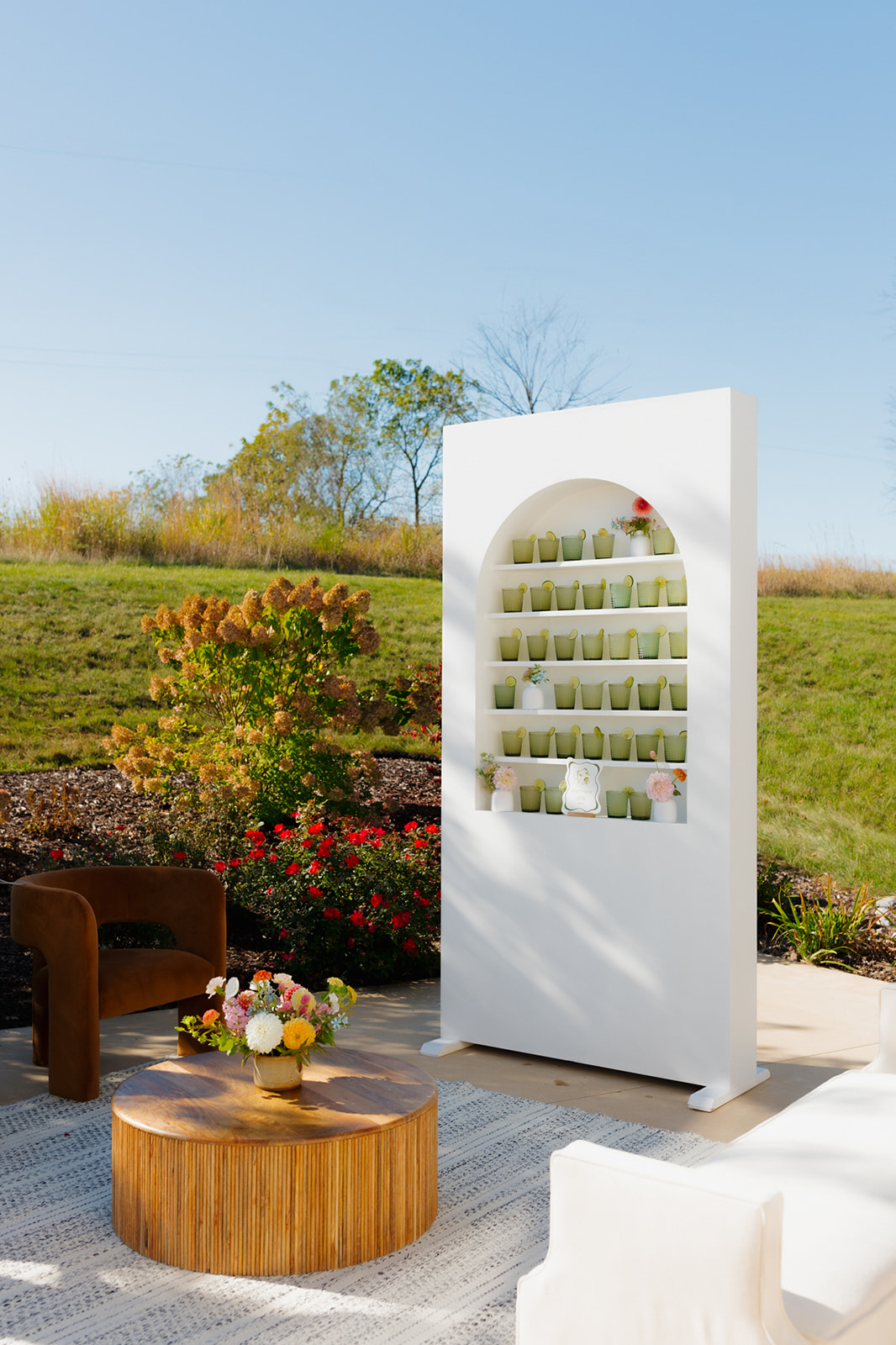 Signature cocktail display with lime-garnished glasses styled on a white shelf, set against lush greenery at a Wisconsin venue.