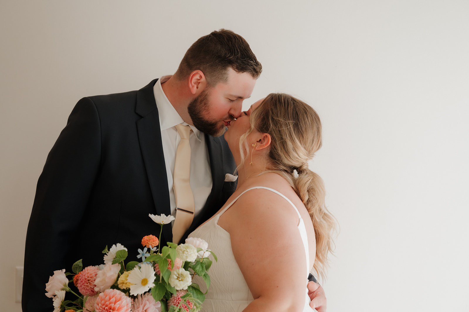 Groom leans in to kiss the bride as she holds a colorful bouquet at their wedding venue in Wisconsin.