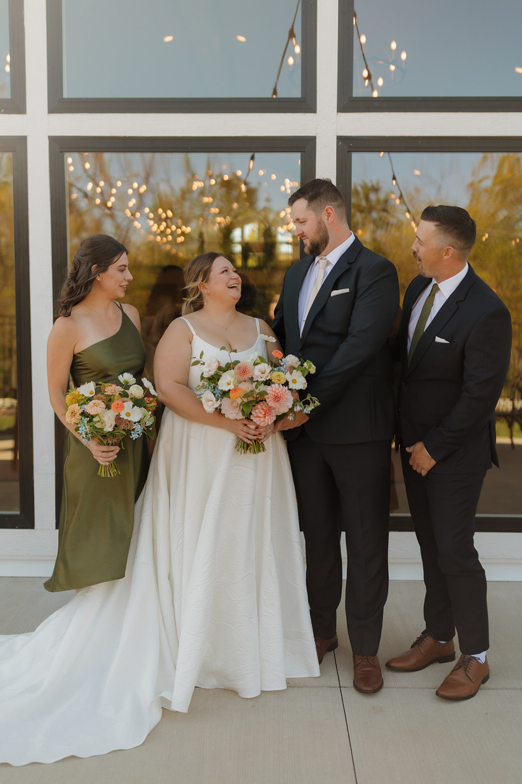 Wedding party laughs together in front of large windows at a wedding venue in Wisconsin.