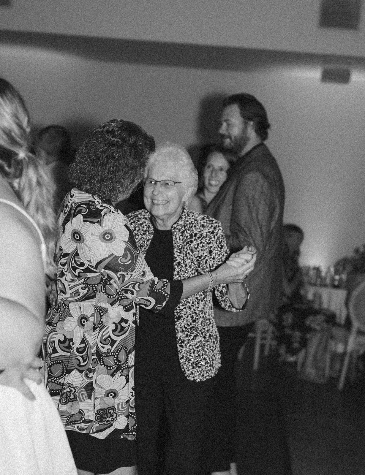 Black and white photo of two guests dancing together at a wedding celebration.