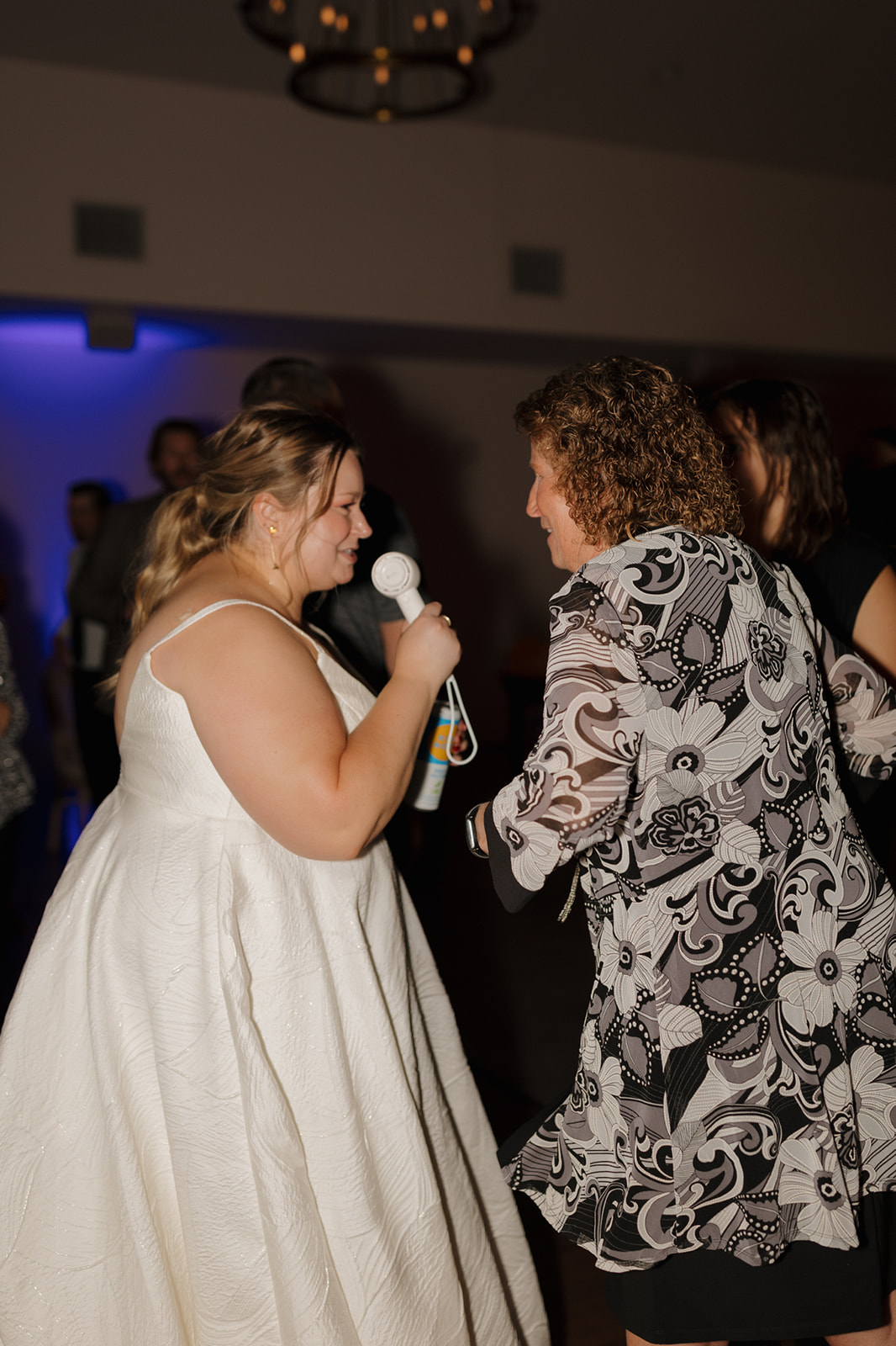 Bride laughs and sings into a mic while dancing with a guest on the dance floor.
