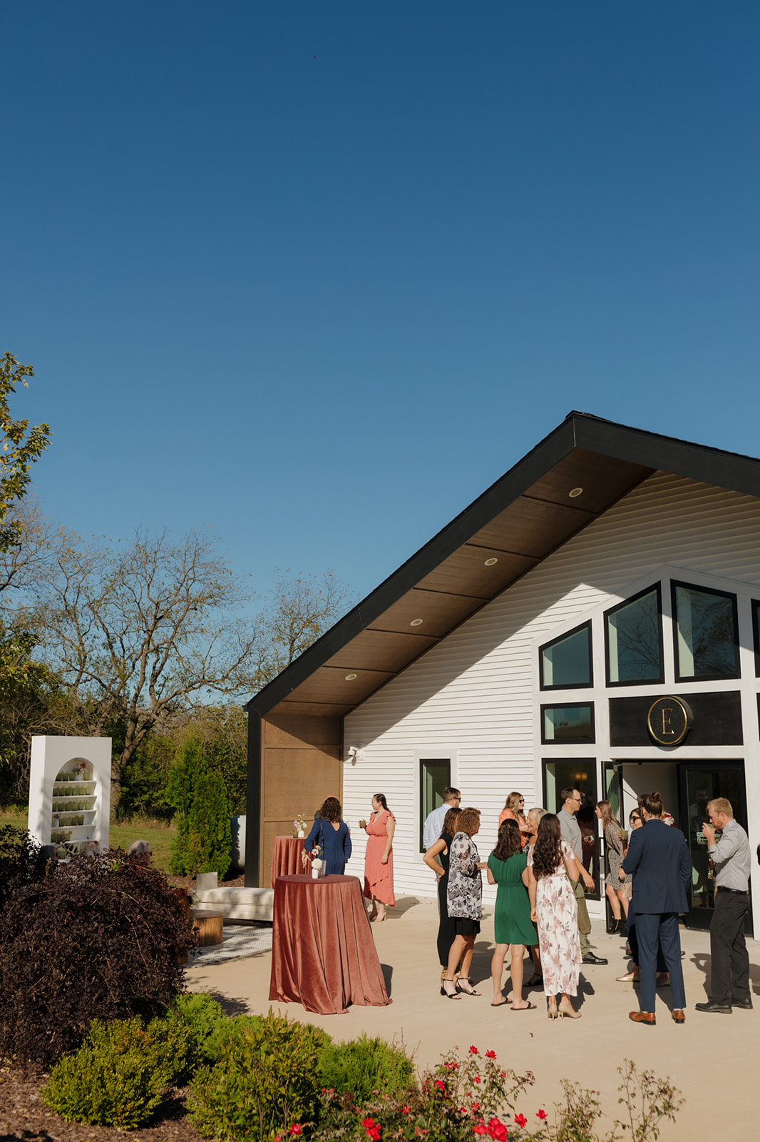 Guests mingling under a clear blue sky outside a stylish wedding venue in Wisconsin, drinks in hand and dressed to the nines.