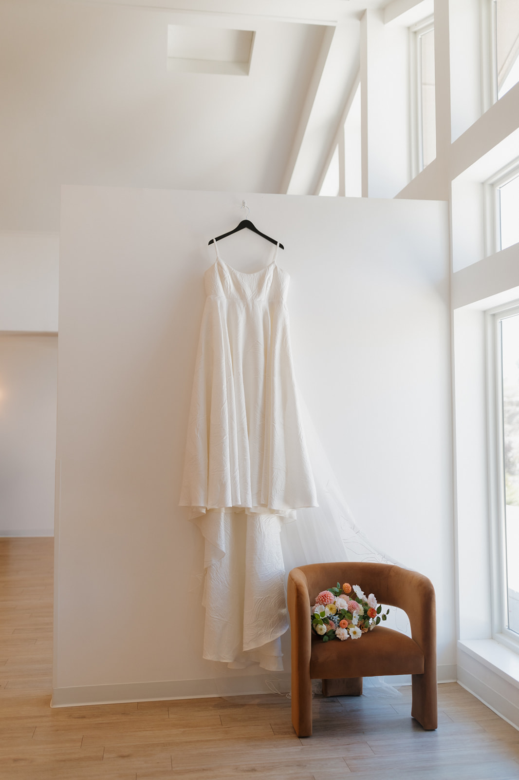 A-line wedding dress hanging in a sunlit corner, with the bride’s bouquet resting on a velvet chair nearby at a Wisconsin venue.