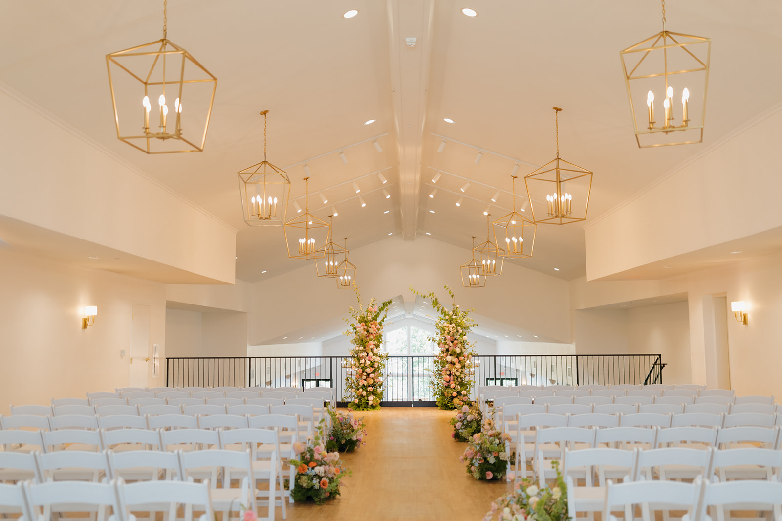 Empty ceremony setup featuring white chairs, floral aisle markers, and gold chandeliers inside a light-filled wedding venue in Wisconsin.
