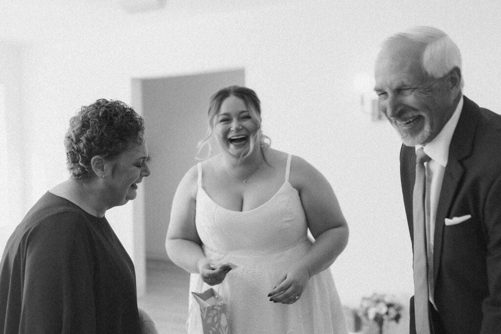 Black and white photo of the bride laughing with her parents, capturing a heartfelt family moment before the ceremony.