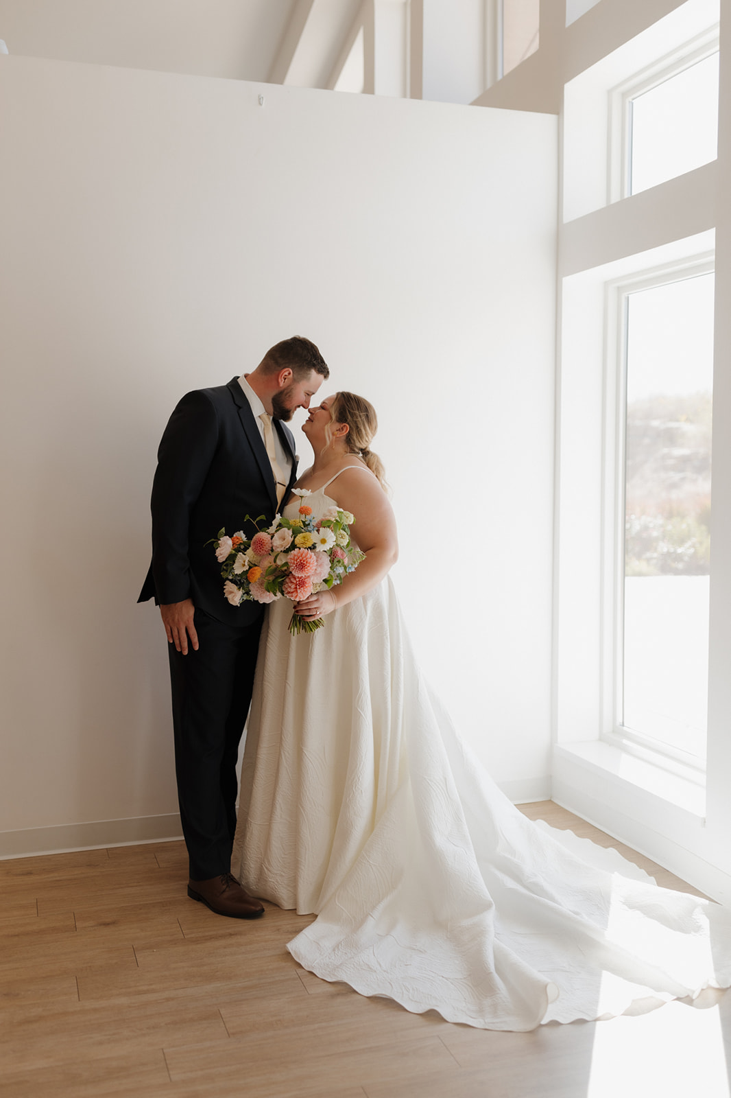 Couple kisses by floor-to-ceiling windows inside a modern Wisconsin wedding venue.