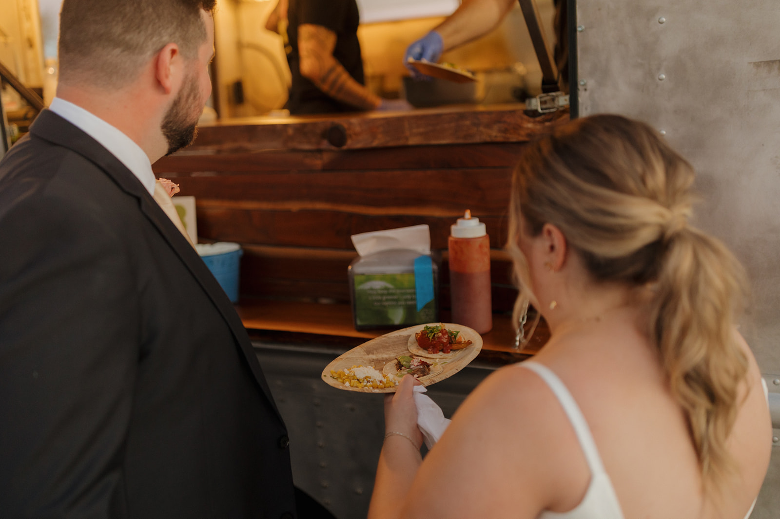 Bride and groom order tacos from a food truck during their outdoor wedding reception.