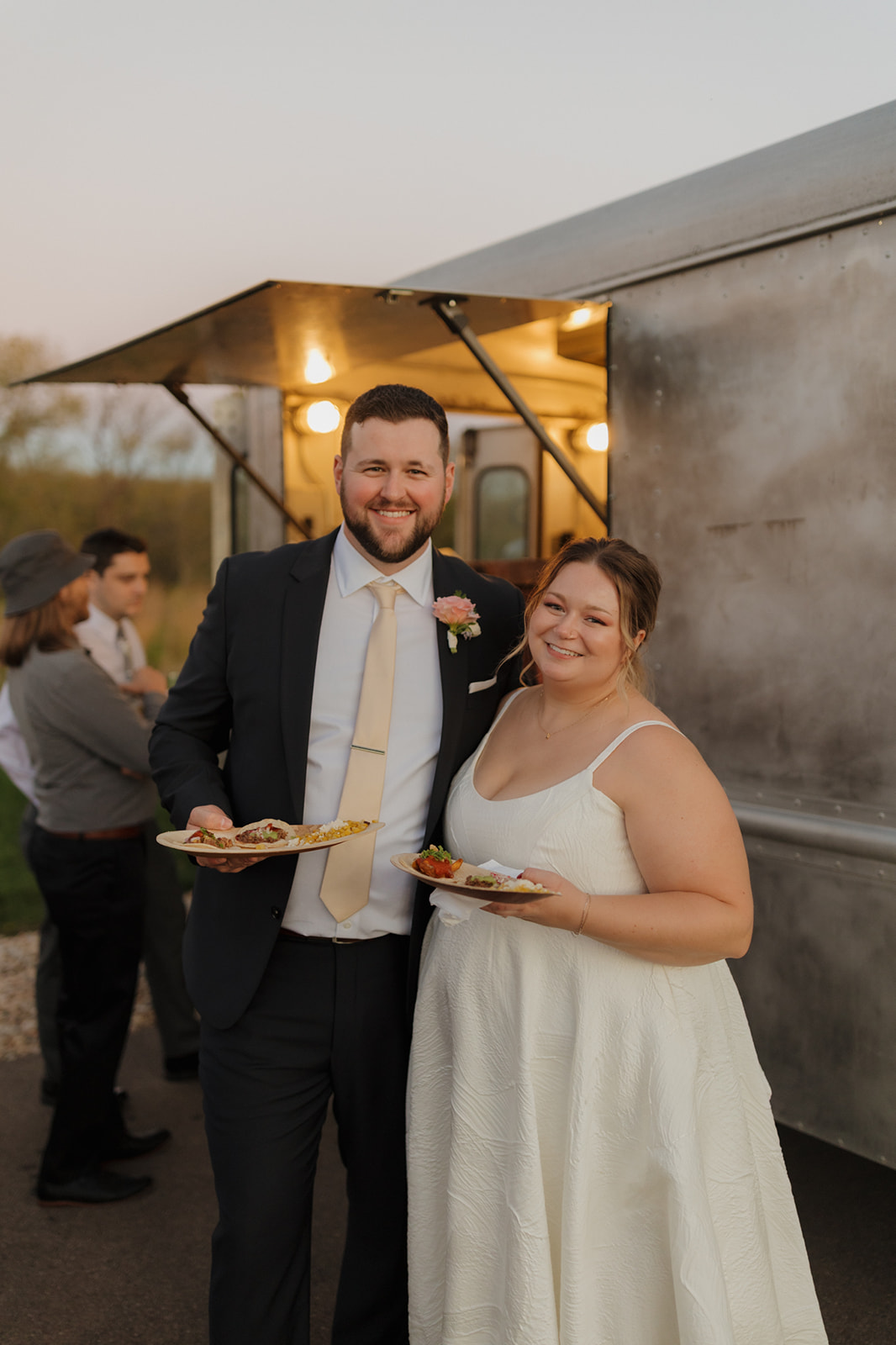 Bride and groom smiling outside a vintage food truck during golden hour at their wedding reception.