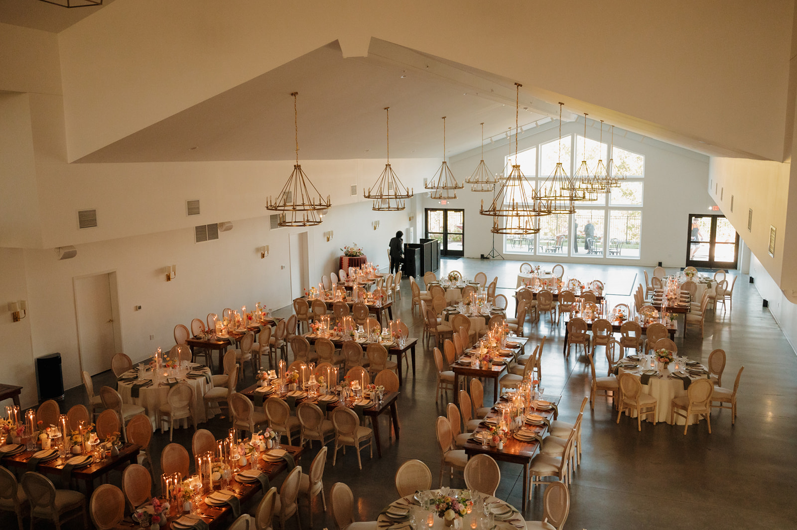 Candlelit reception space with long farmhouse tables and blush velvet chairs inside a spacious Wisconsin wedding venue.