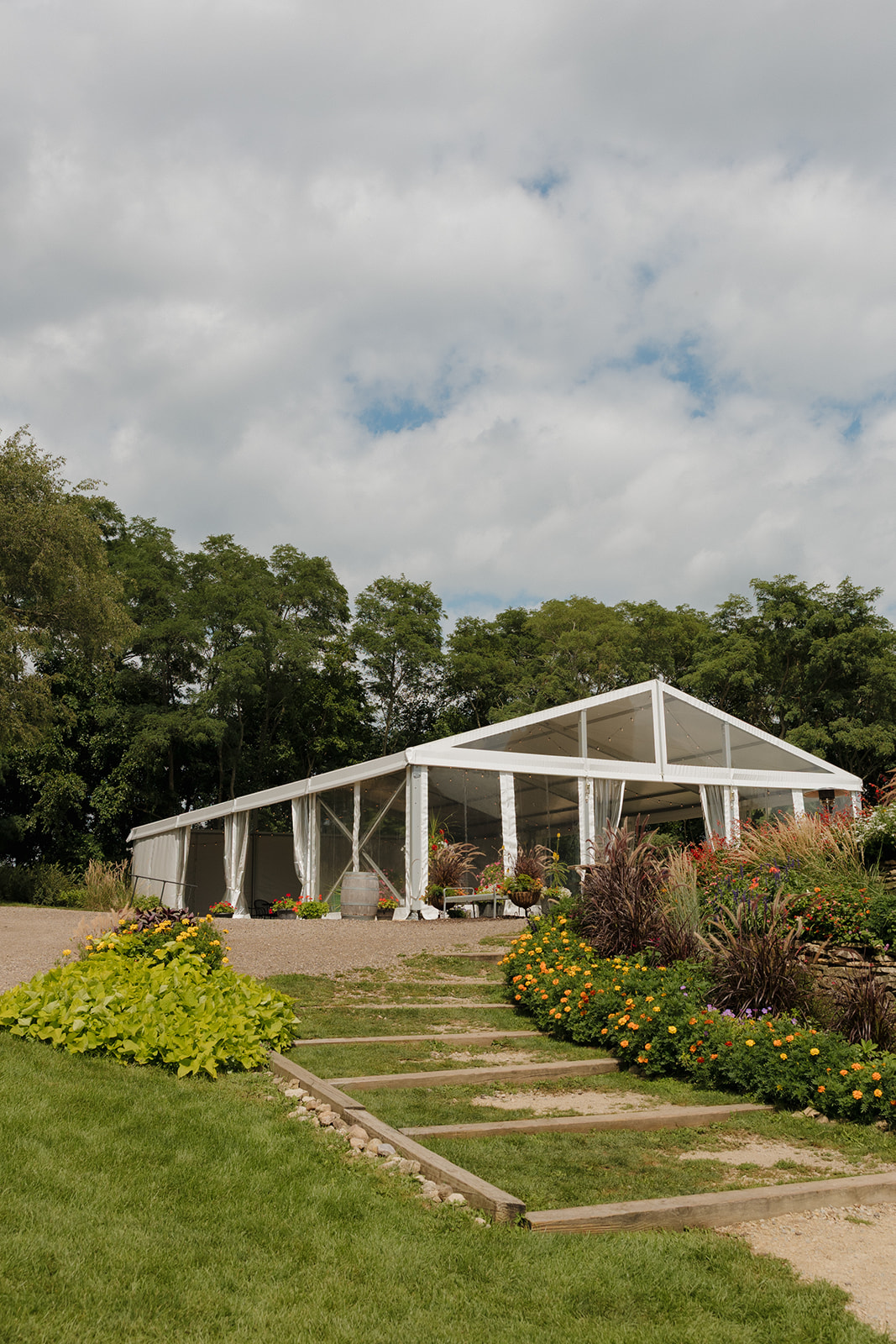This floral-filled garden path leads to a stylish clear-top tent—an elegant pick among Madison wedding venues for modern outdoor receptions.