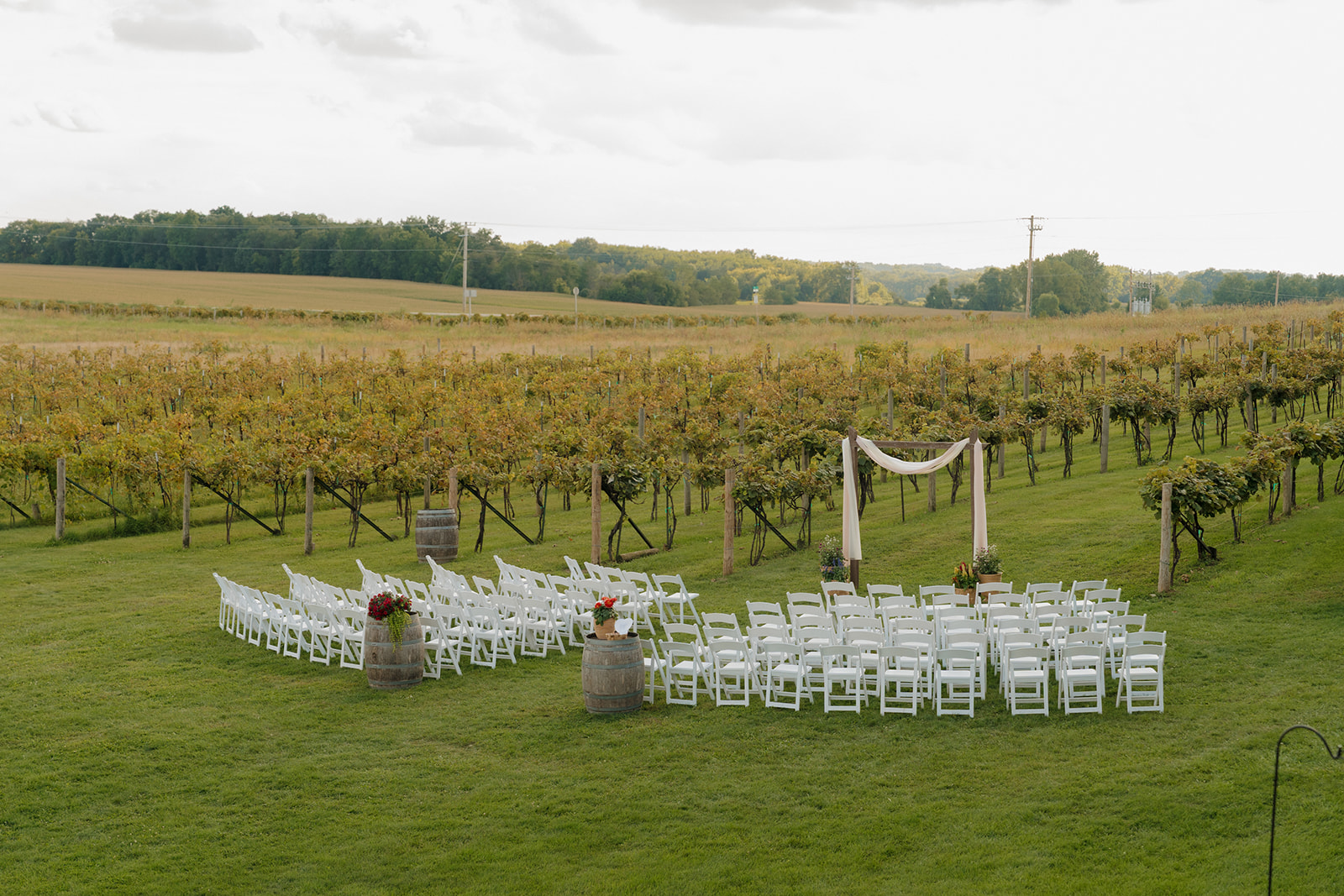 Ceremony setup with vineyard rows, white chairs in a half-moon formation, and wine barrels—picture-perfect for Madison wedding venues.