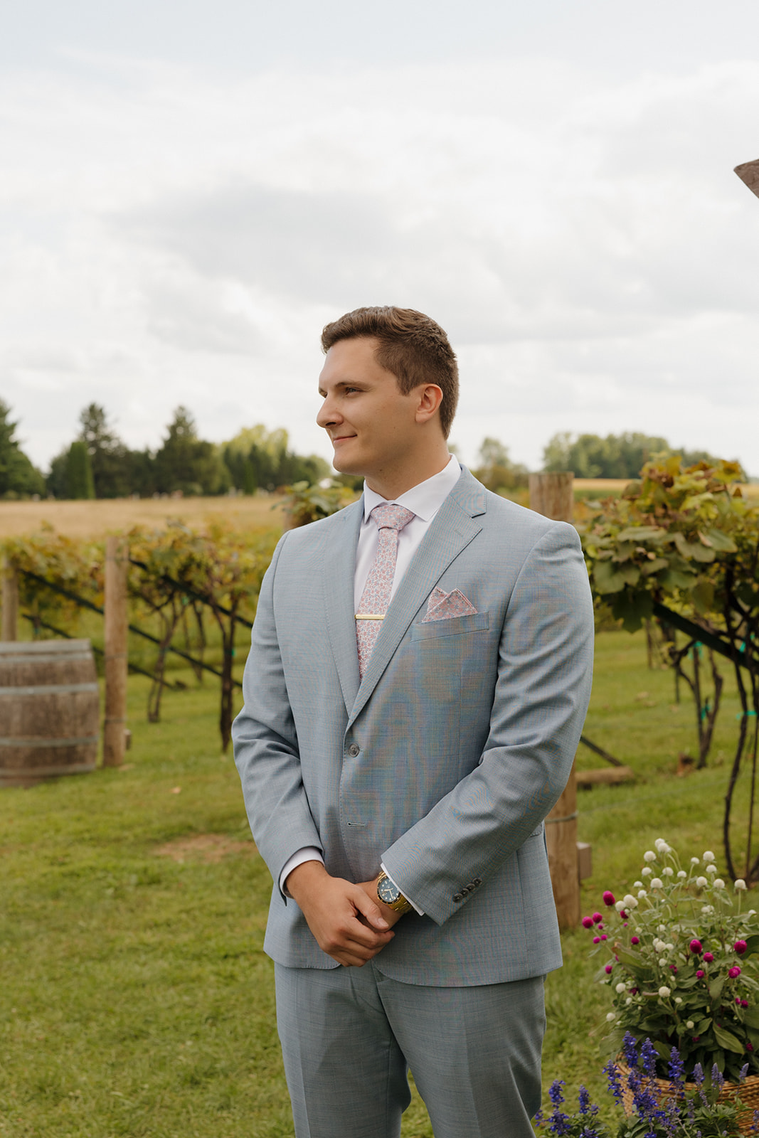 The groom stands smiling in a vineyard aisle, one of the most peaceful and romantic spots among Madison wedding venues.
