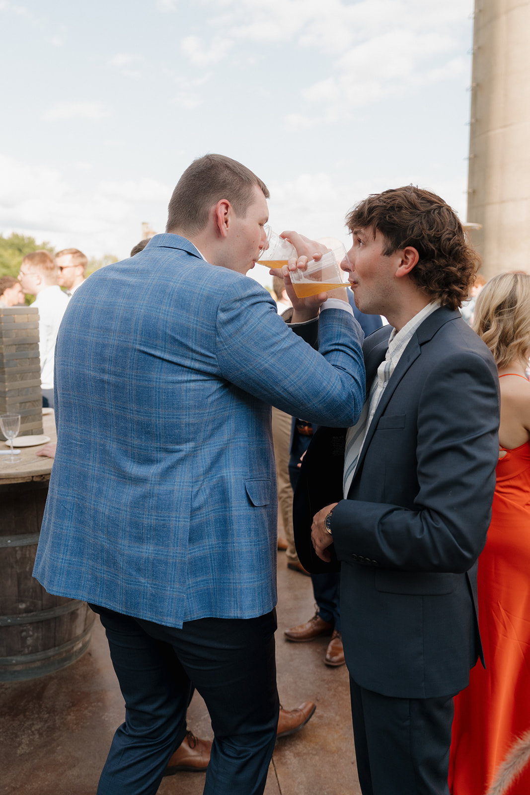Cheers to love and cold beers—two groomsmen share a celebratory sip with friends under sunny skies.