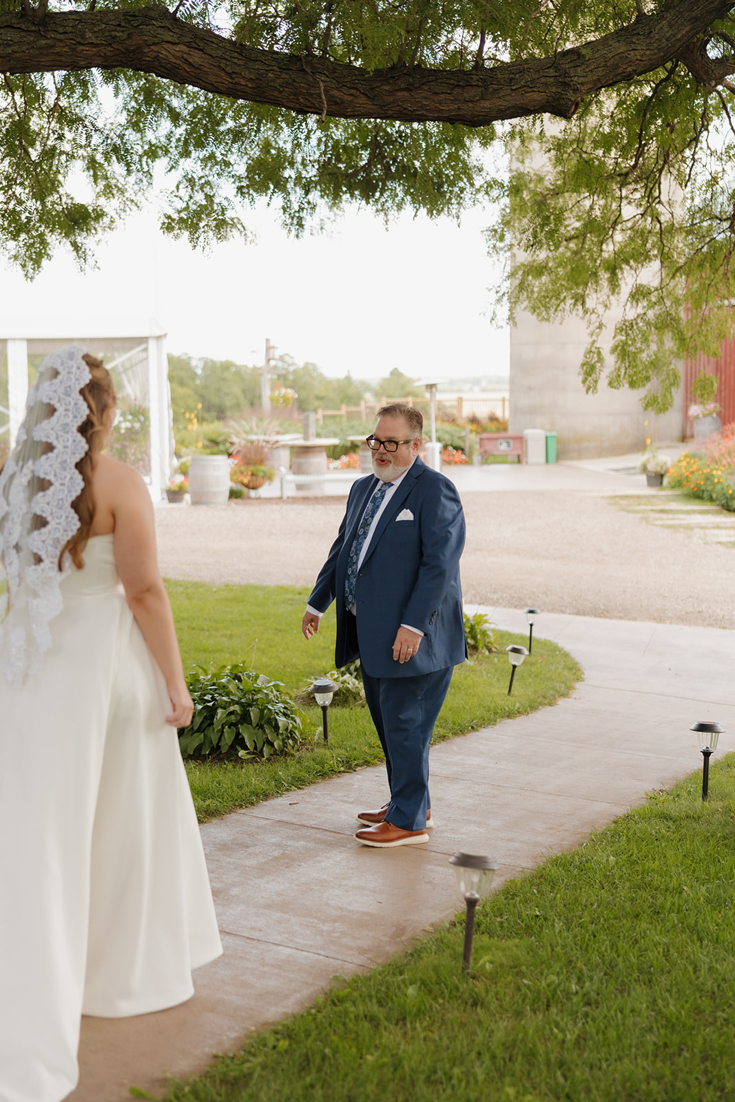 An emotional first look between father and daughter on the shaded path of a Madison wedding venue, surrounded by greenery and charm.